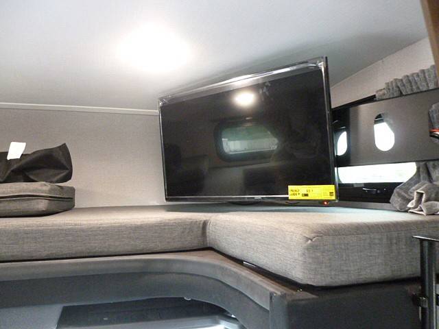 Inside an RV rental, a flat-screen TV is mounted above a comfortable gray bunk bed or seating area, ready for your trip.. Forest River Sunseeker 2020