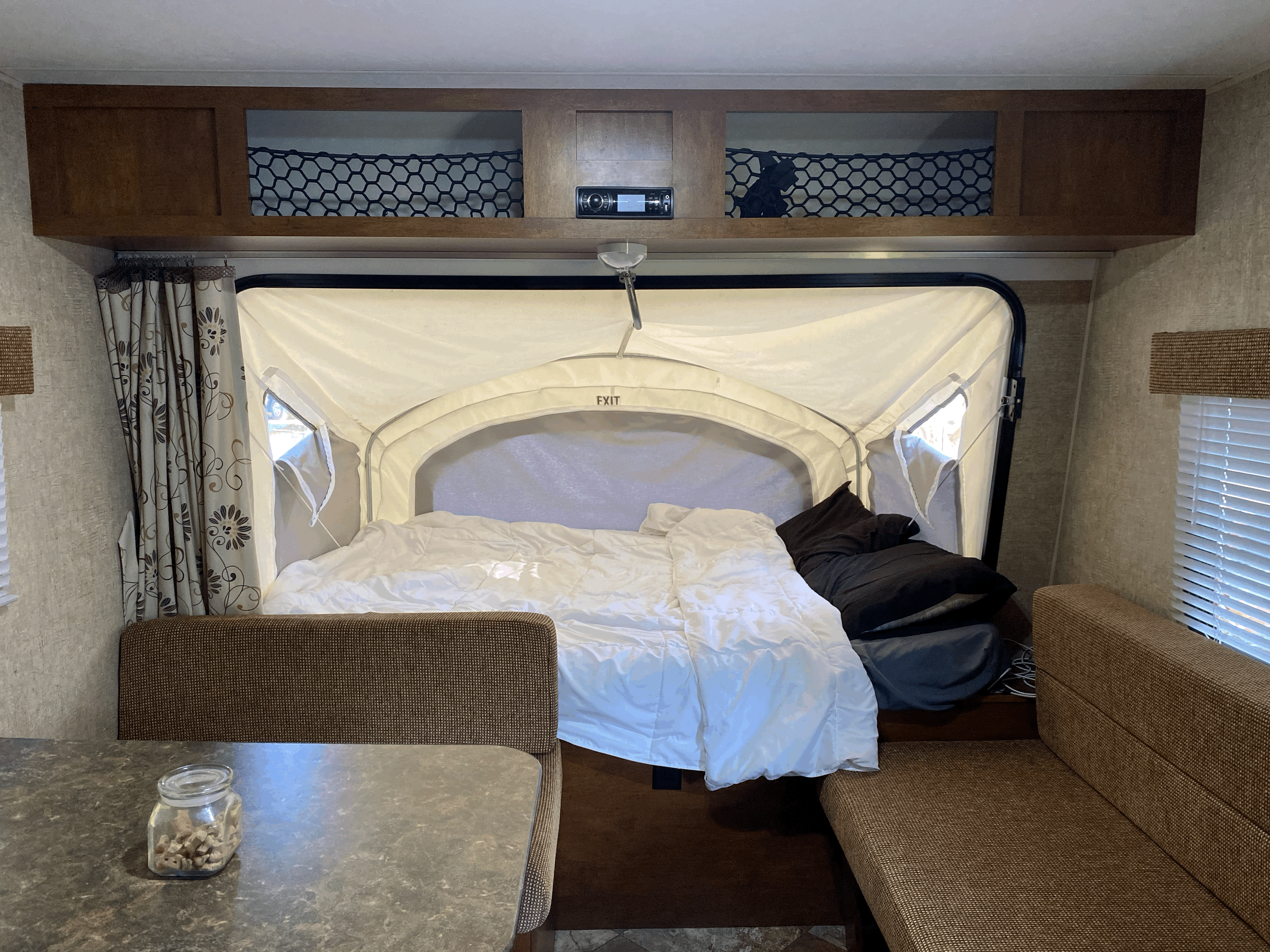 Interior of a compact RV rental featuring a comfortable pop-out bed, dinette with seating, and overhead storage nets.. K-Z Manufacturing Sportsman Classic 2015