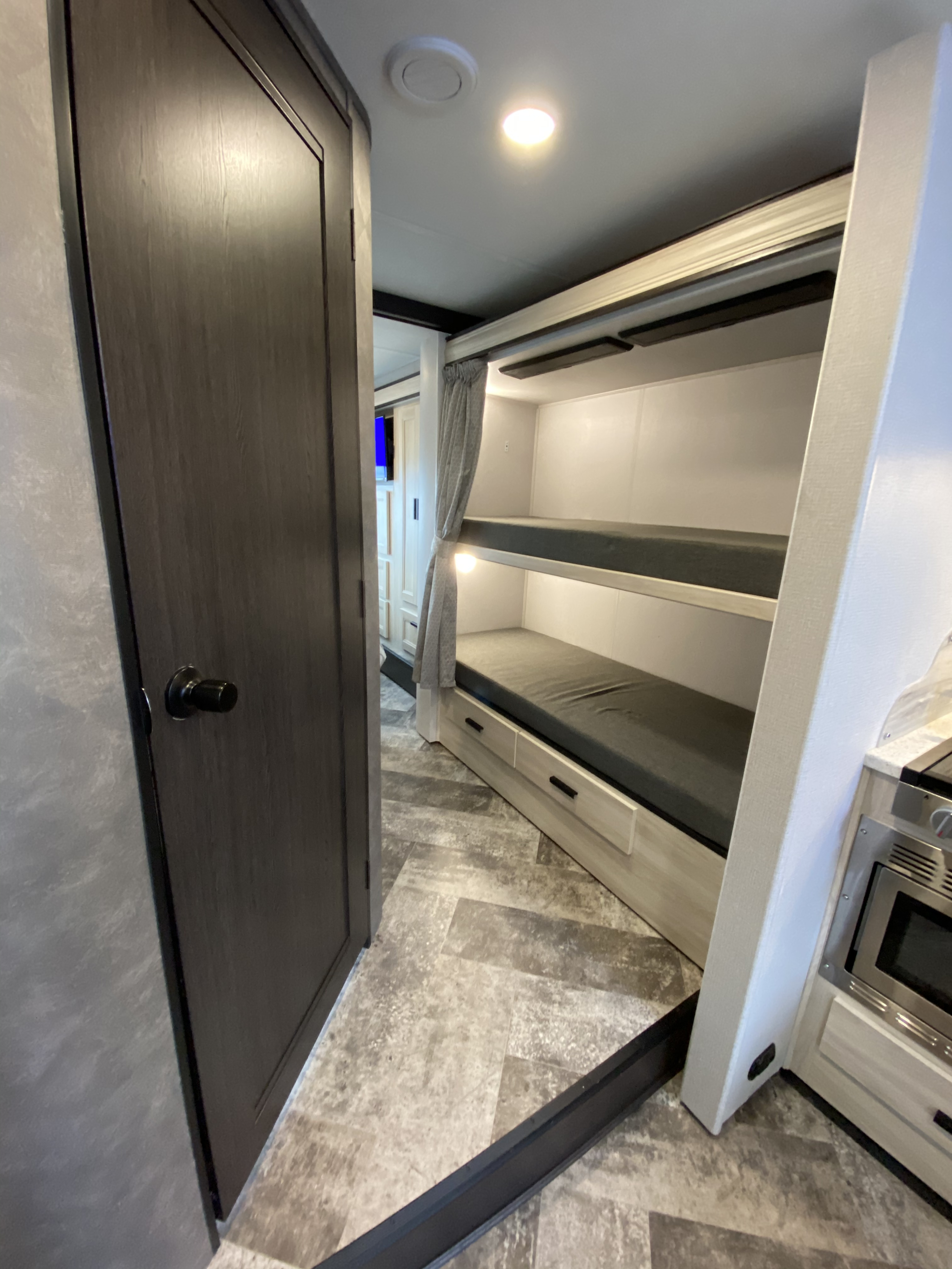 Inside an RV rental, a dark door opens to a hallway with bunk beds, a privacy curtain, and a glimpse of the kitchen.. Forest River Forester 2021