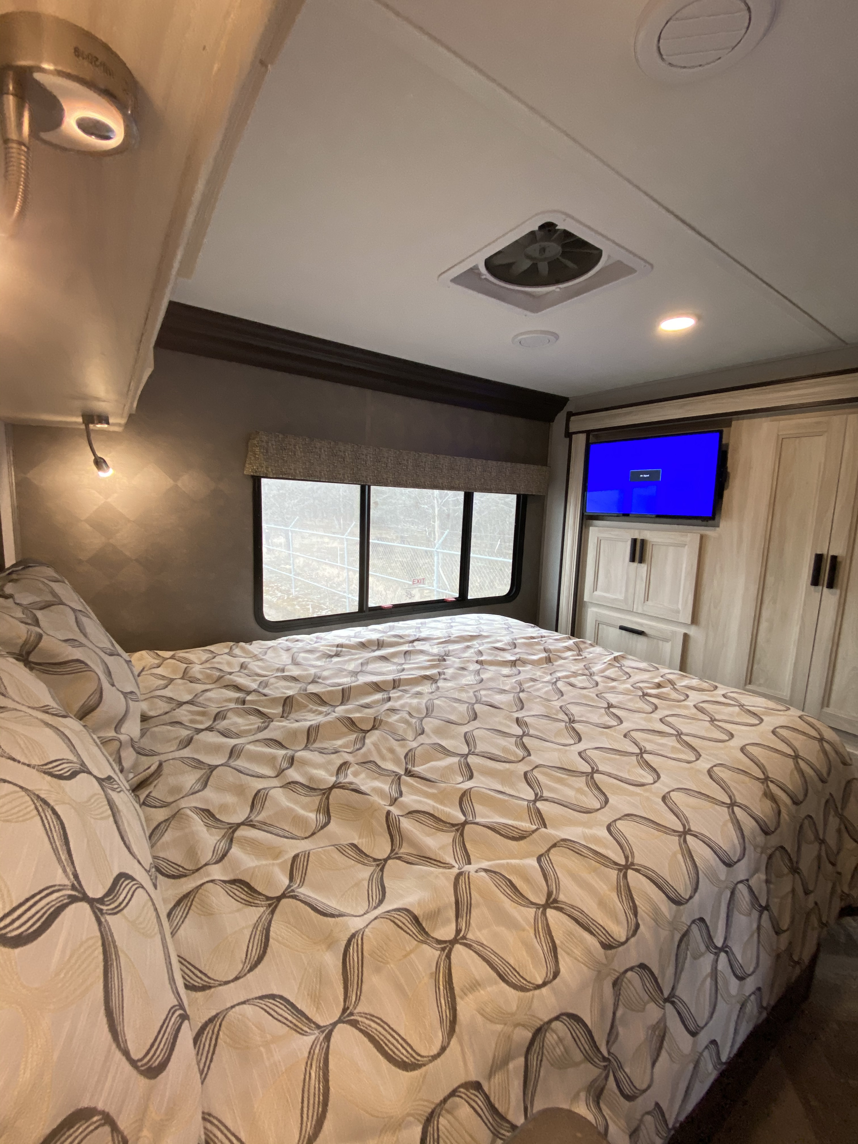 Inside an RV rental bedroom: cozy bed with patterned linens, TV, cabinetry, and window view.. Forest River Forester 2021