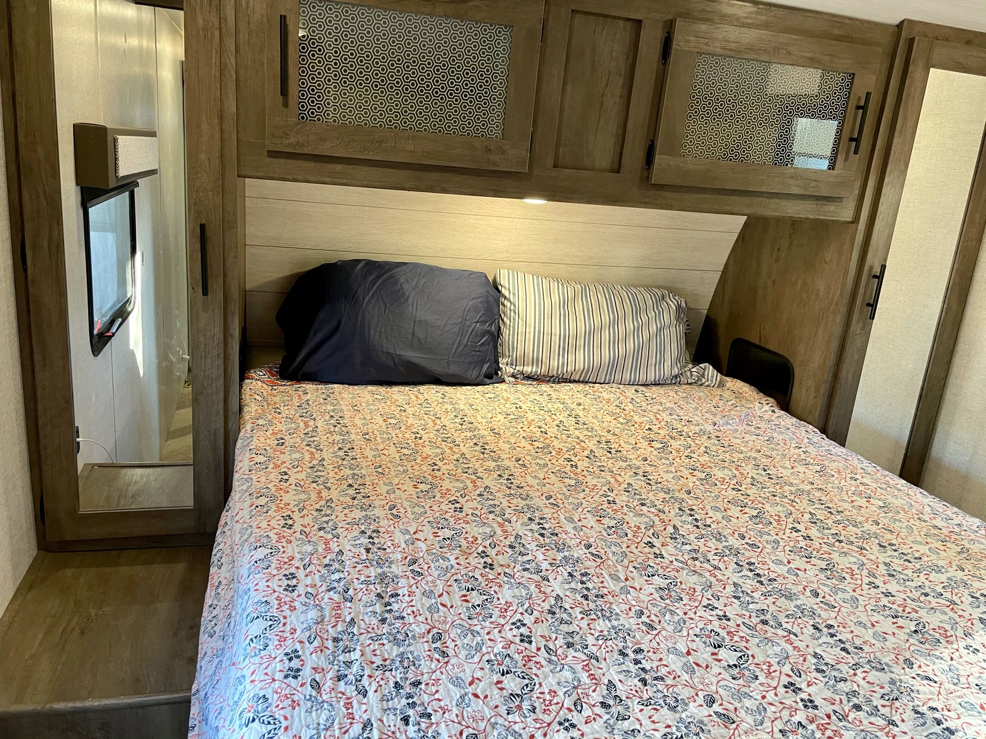 RV rental bedroom: a comfy bed with a floral quilt, overhead cabinets, and a side mirror for your travels.. Forest River Salem 2020