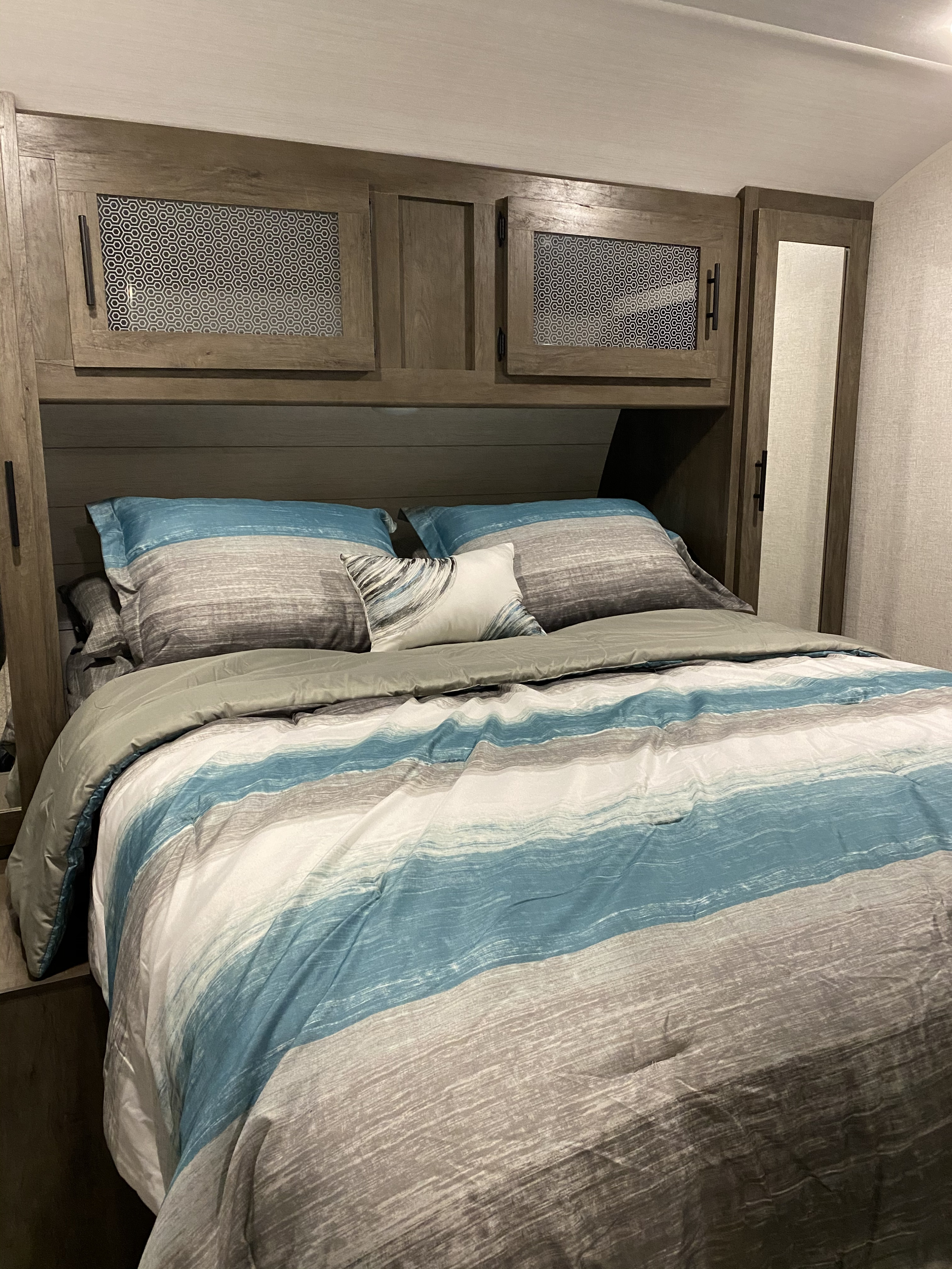 Cozy RV rental bedroom featuring a bed with striped blue, gray, and white bedding, and wood cabinetry overhead.. Forest River Salem 2021
