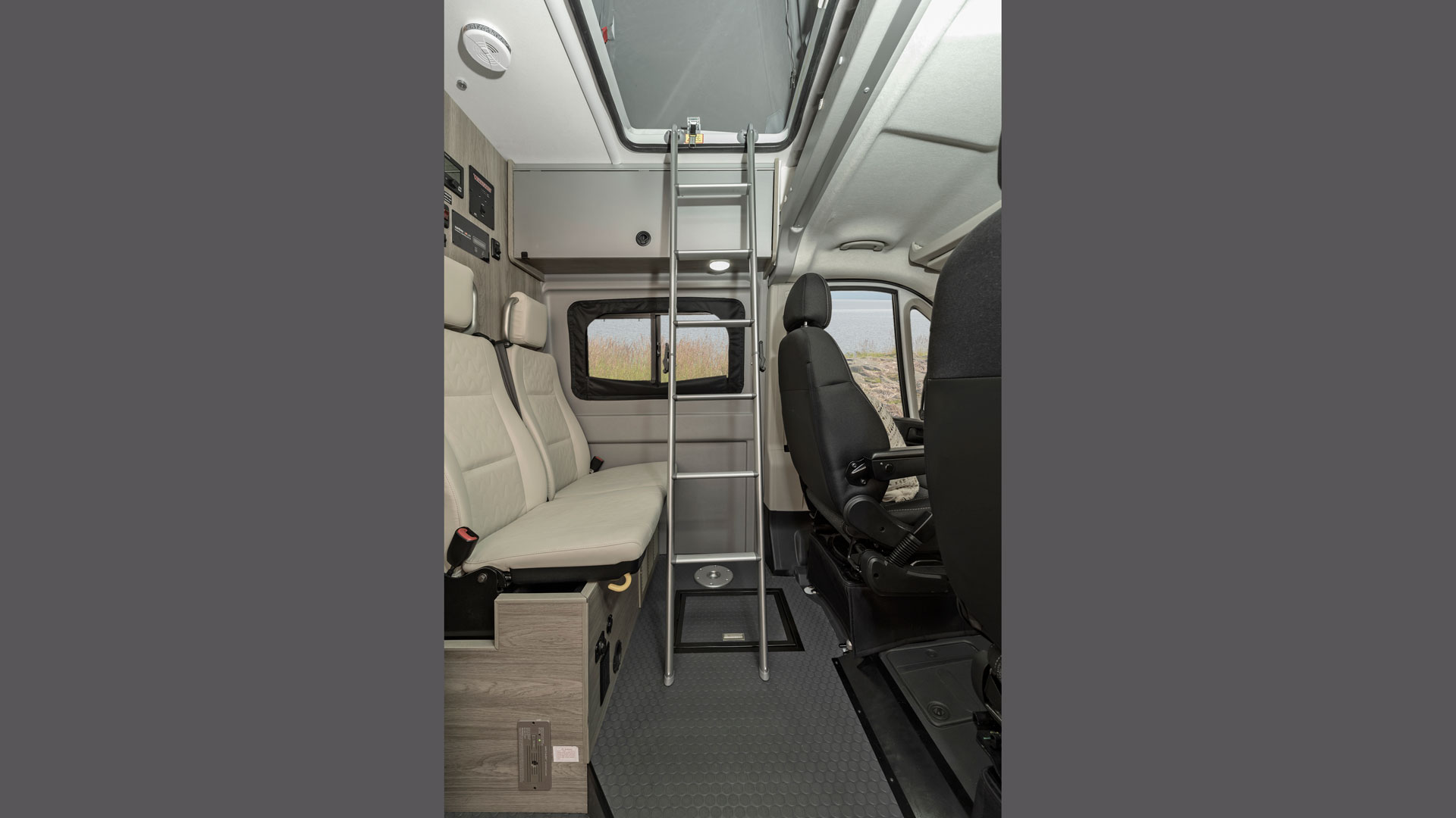 Interior of an RV rental: Features a ladder to a top bunk, comfortable seating, and a scenic window view.. Winnebago Solis 2021
