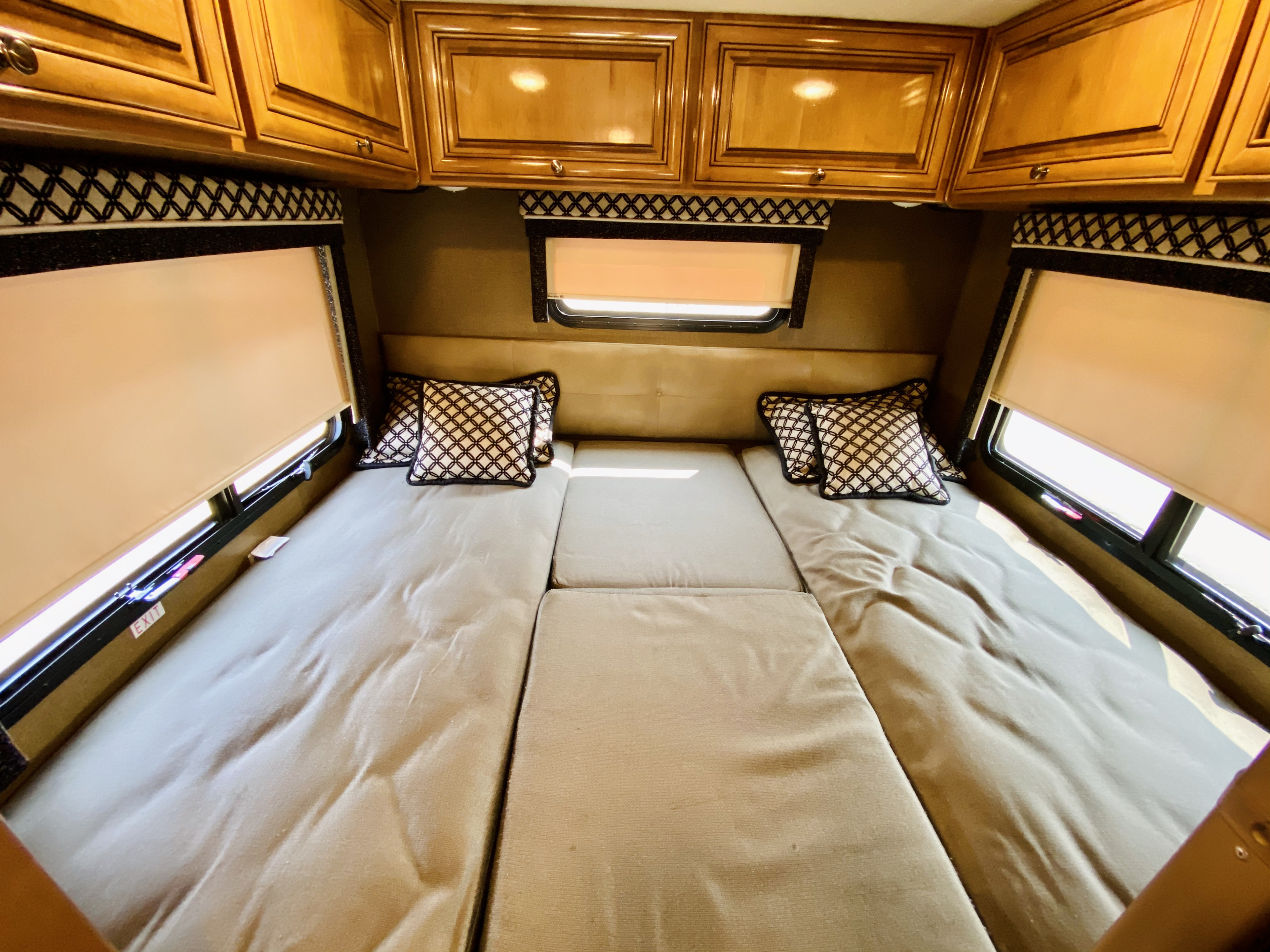 Comfortable RV rental bedroom featuring a modular bed, overhead wood cabinets, and pull-down window shades.. Thor Motor Coach Siesta 2017
