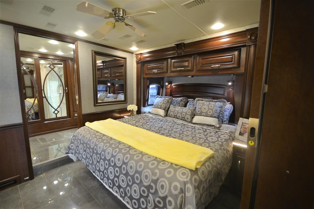 A luxurious RV bedroom with a large bed, dark wood furnishings, and overhead storage, ideal for your next RV rental trip.. Entegra Coach Anthem 44B 2017