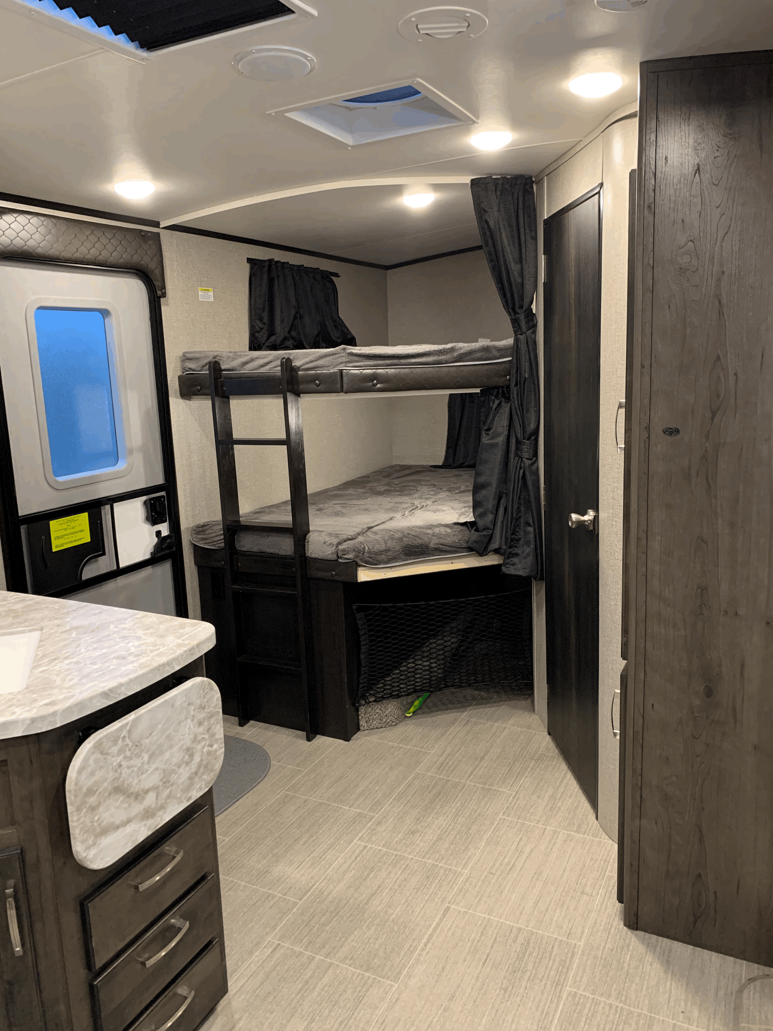 RV rental interior: bunk beds, bright blue door window, compact counter, and overhead lighting.. Jayco White Hawk 2021