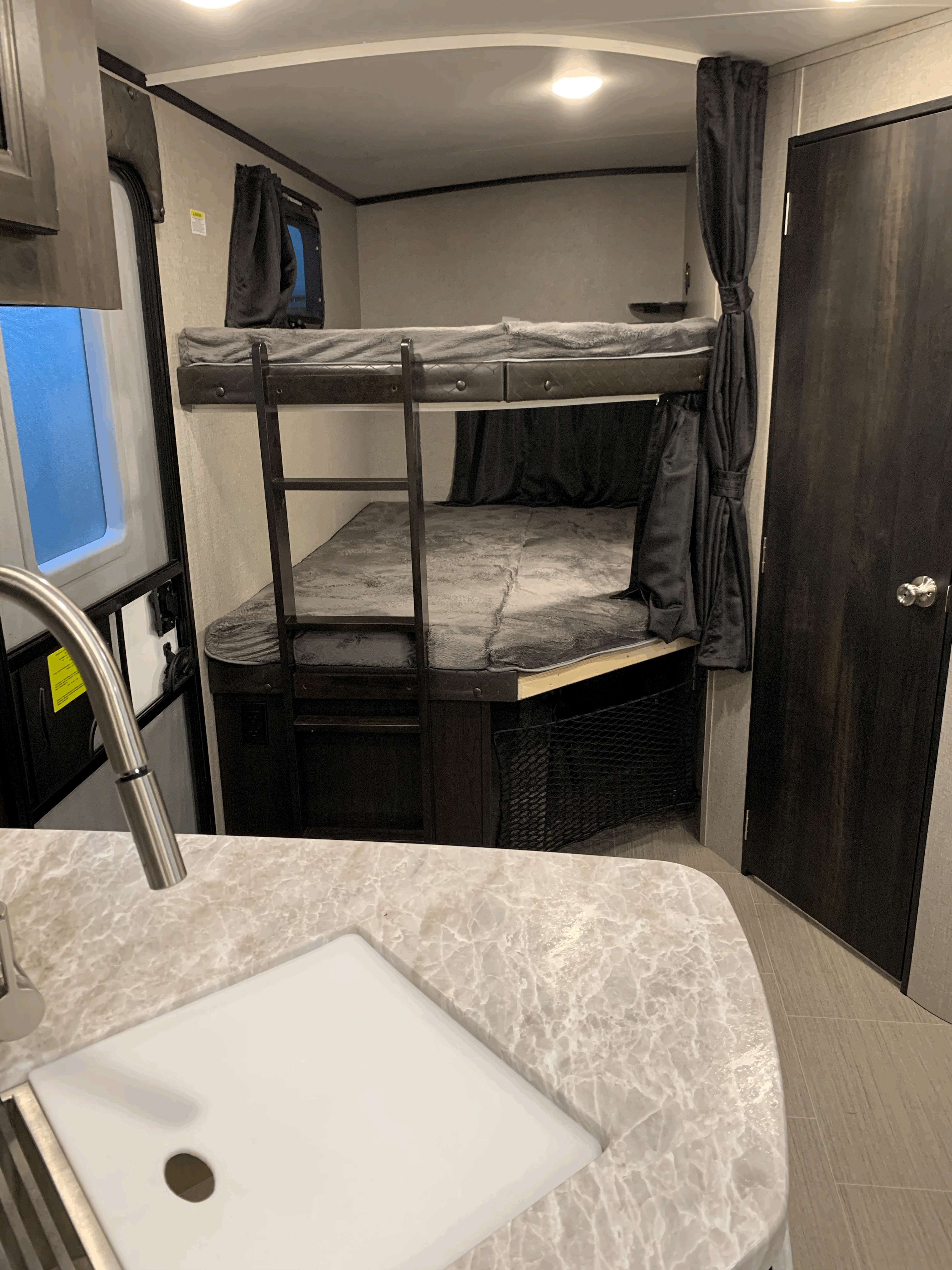 RV rental interior showcasing bunk beds with ladder & privacy curtains, a kitchen sink, and a nearby entry door. Efficient use of space.. Jayco White Hawk 2021