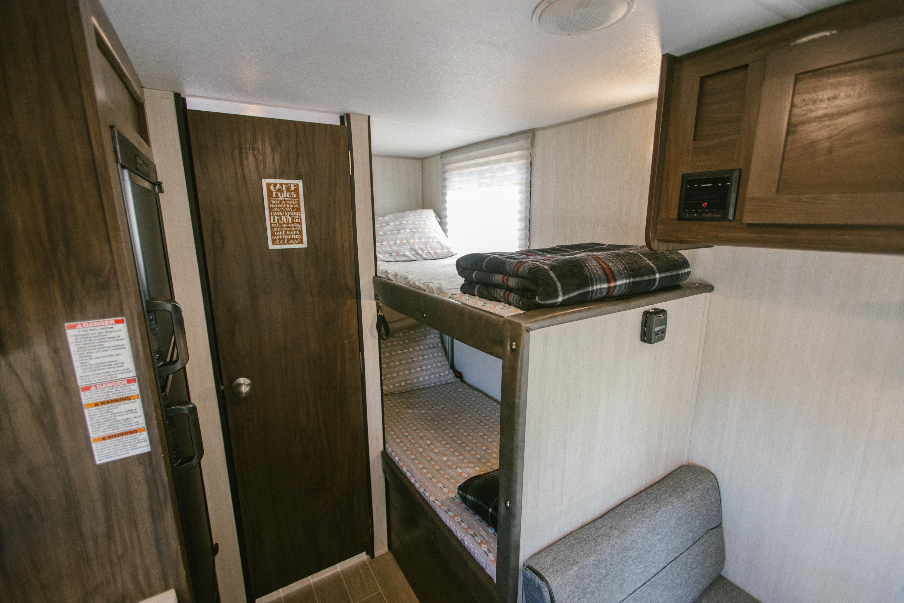 An RV rental interior with comfortable bunk beds, a plaid blanket, and a door featuring "CAMP rules" signage.. Forest River Cherokee Wolf Pup 2020