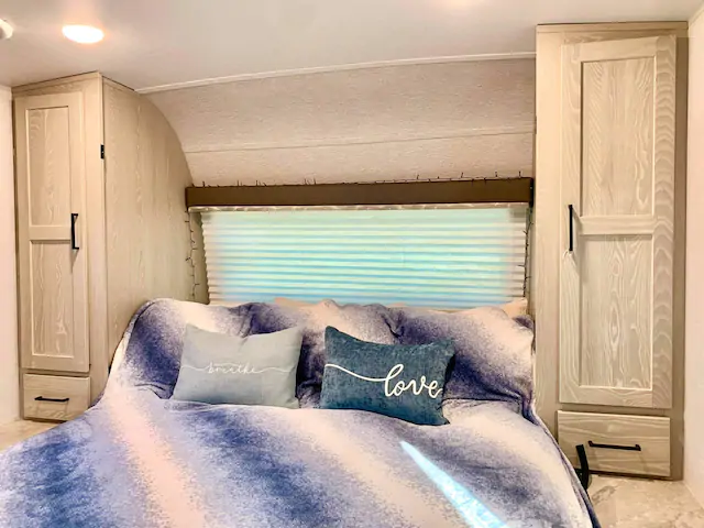 Cozy RV rental bedroom featuring a bed with blue bedding, "breathe" and "love" pillows, and light wood cabinets.. Forest River Rockwood Mini Lite 2021