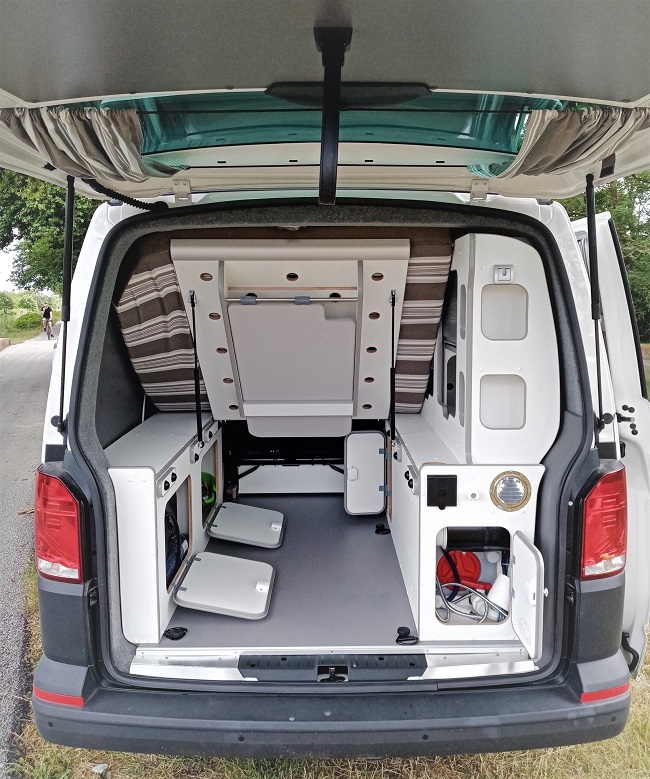 Inside a modern rv rental camper van, showing a versatile modular interior with a bed, storage, and utility access from the open tailgate.. Volkswagen Transporter T6.1 2021