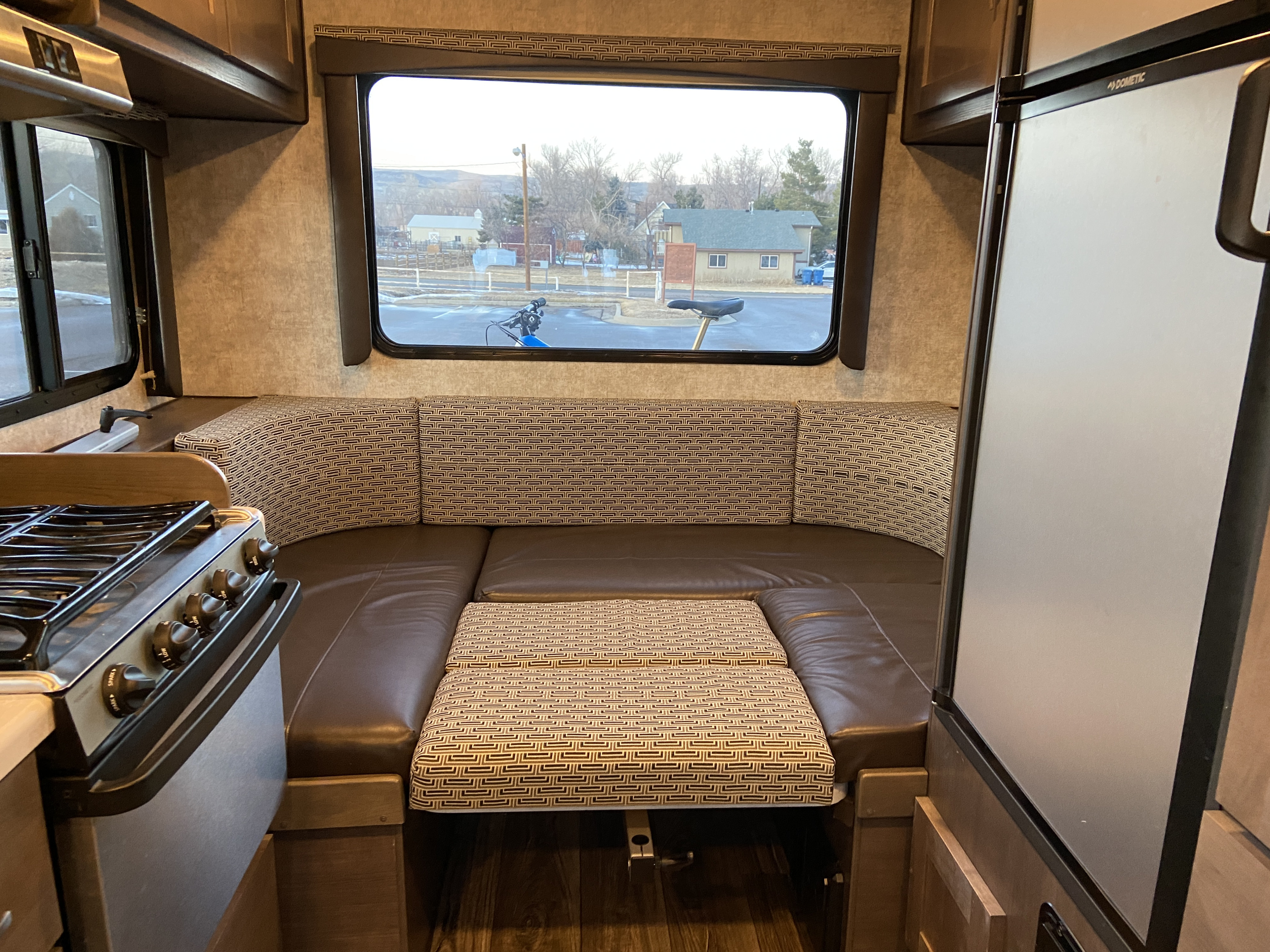 RV rental dinette area featuring brown leatherette seats, patterned cushions, stove, and fridge for your trip.. Alp Adventurer 19RD 2019