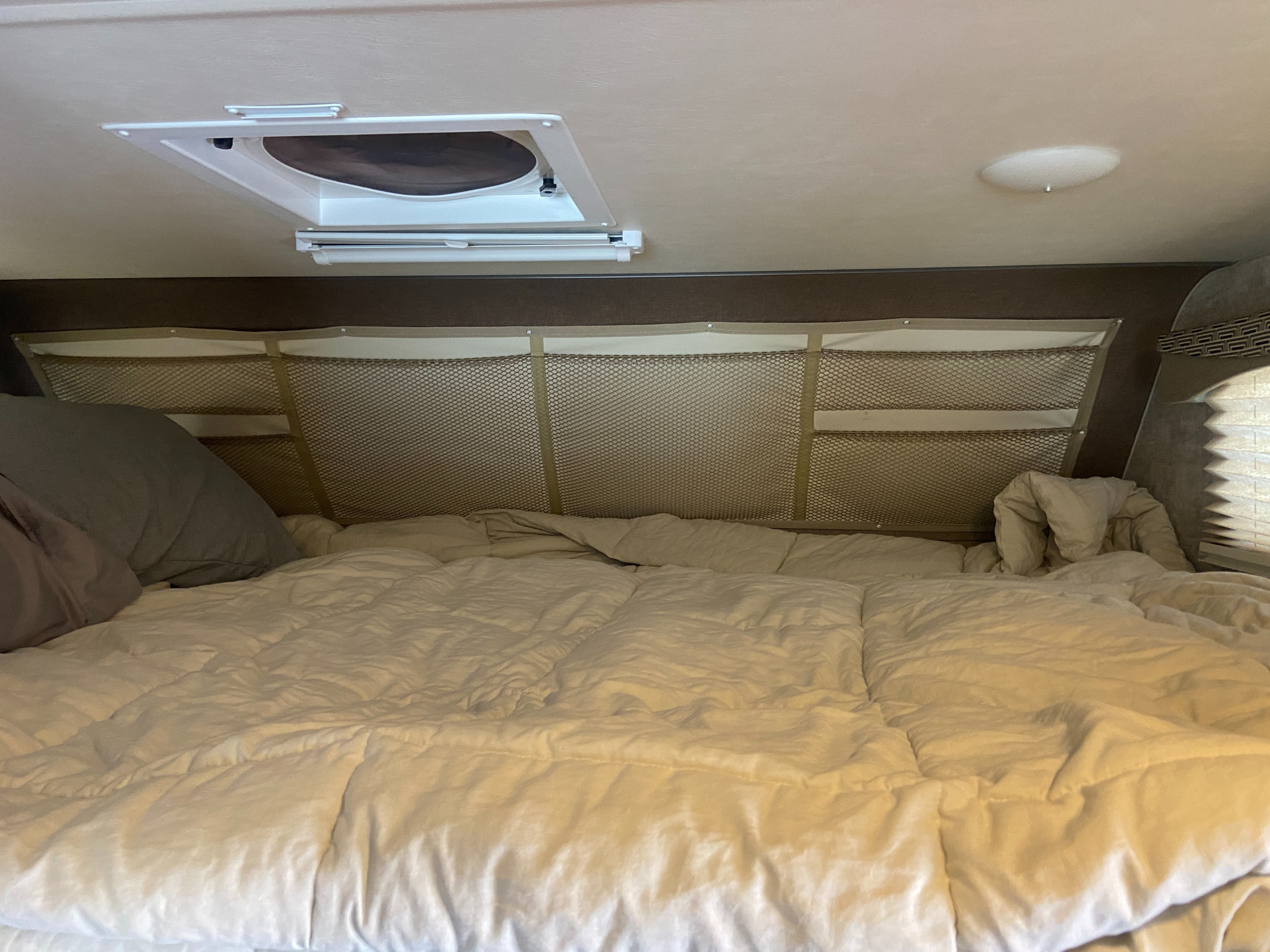 Cozy sleeping area in an RV rental, featuring a comfortable bed, overhead storage nets, and a ceiling vent.. Alp Adventurer 19RD 2019