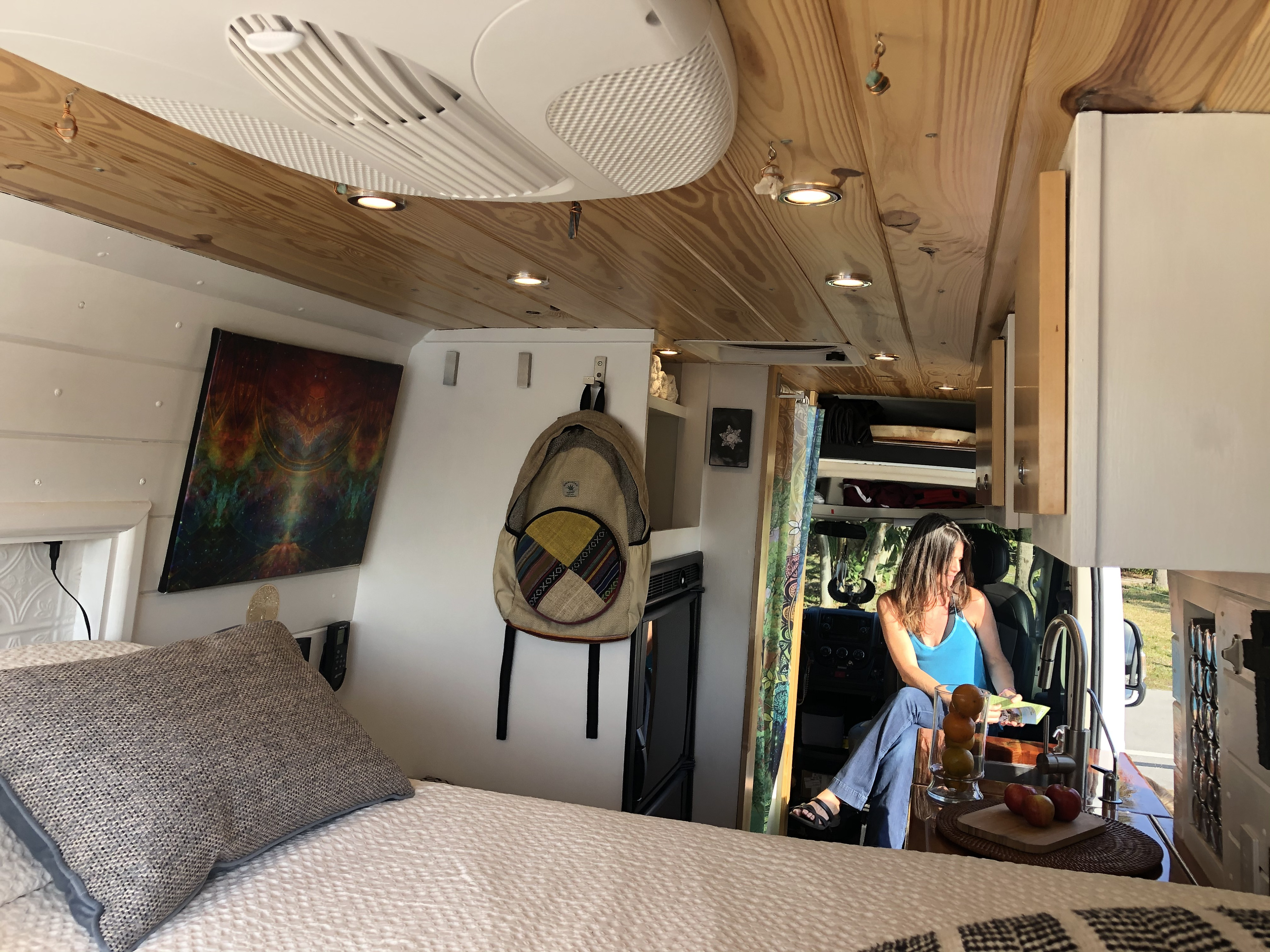 This RV rental's interior boasts a cozy bed, wood ceiling, and a woman relaxing near the compact kitchen and integrated cab area.. Dodge Promaster 3500 2018