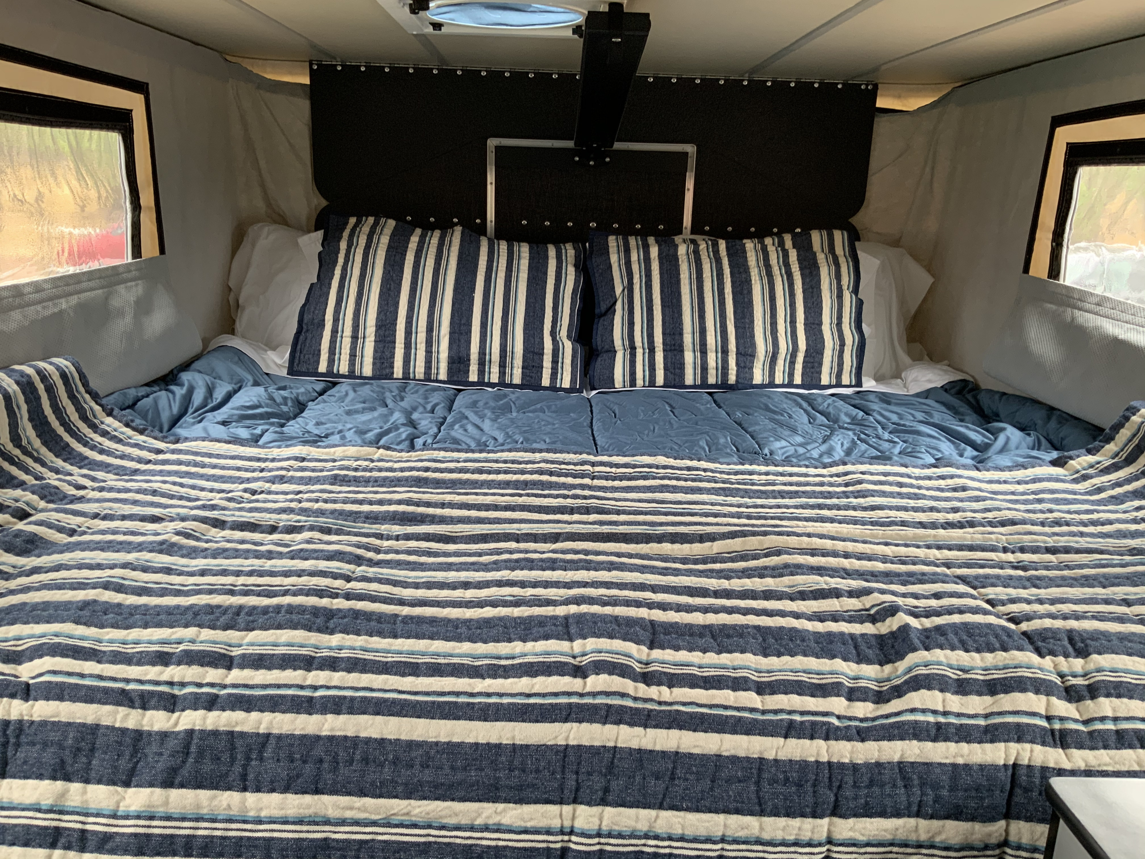 Step into comfort with this RV rental's cozy bedroom. Features blue & white striped bedding, pillows, & windows, perfect for travel.. Four Wheel Campers Other 2017