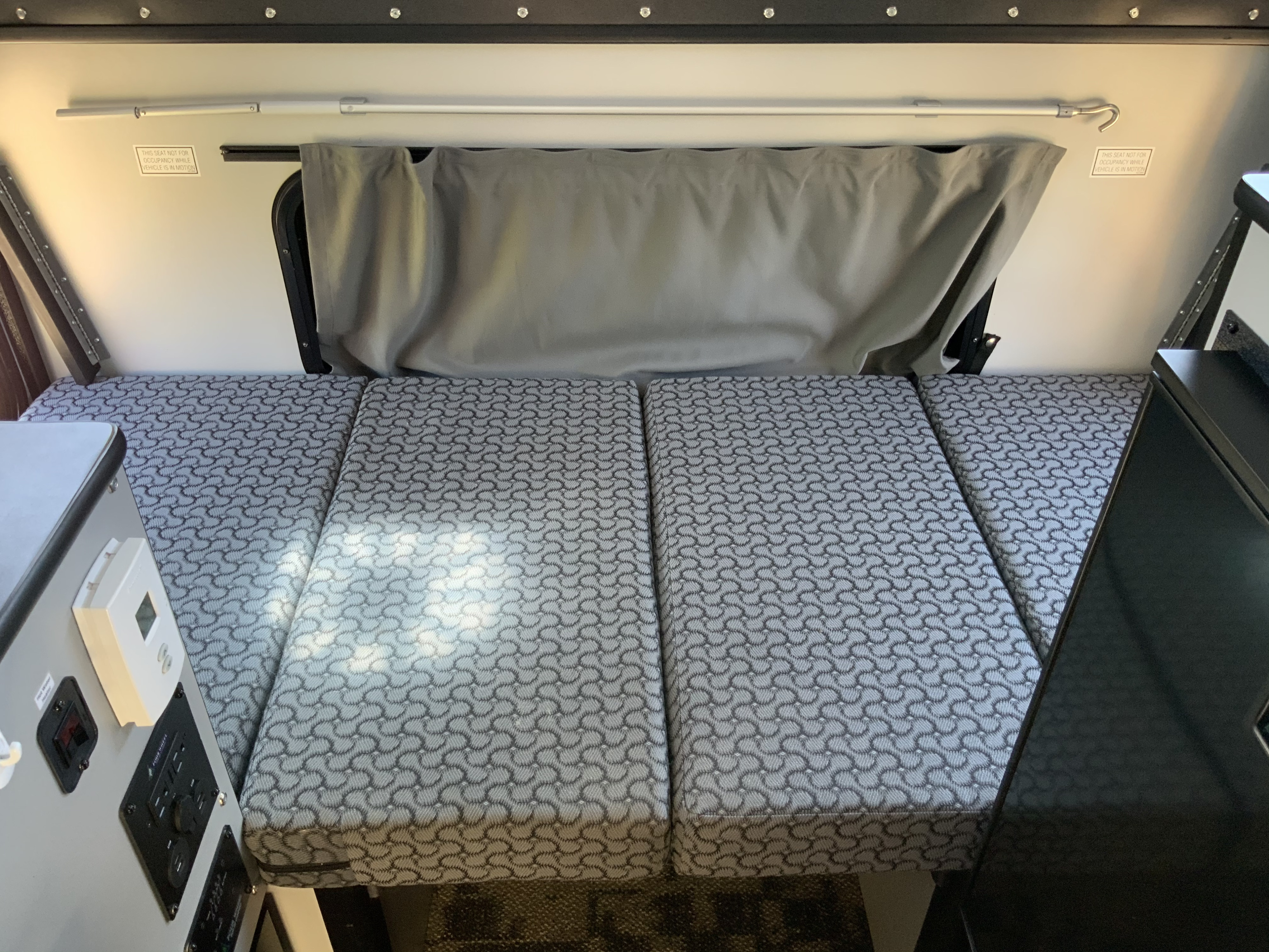 RV rental interior: View of the convertible bed/seating area with patterned cushions, window, and control panel. Warning labels visible.. Four Wheel Campers Other 2017