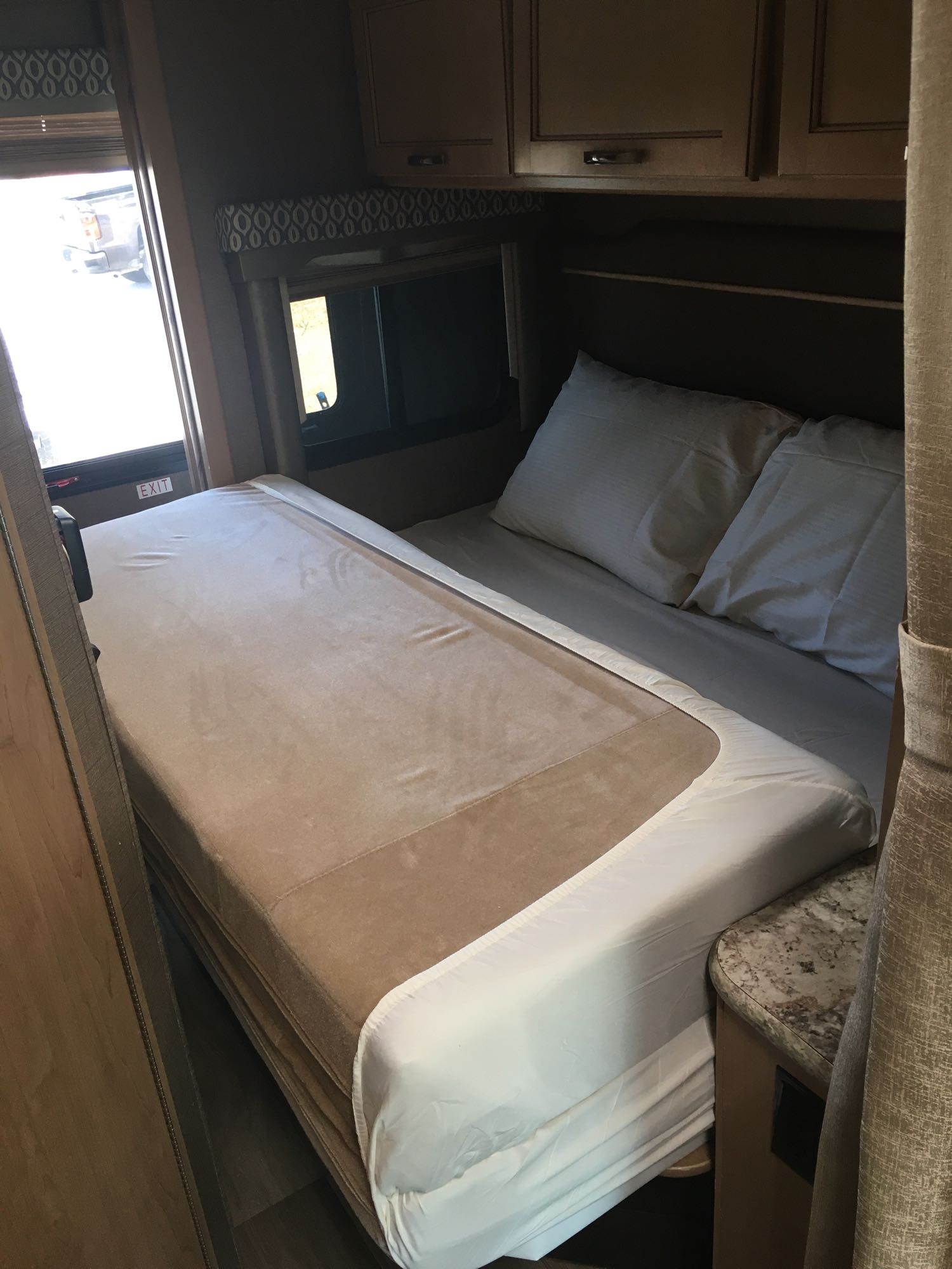 Cozy RV rental bedroom featuring a convertible bed with white linens and ample overhead storage, perfect for travel.. Thor Freedom Elite 2018