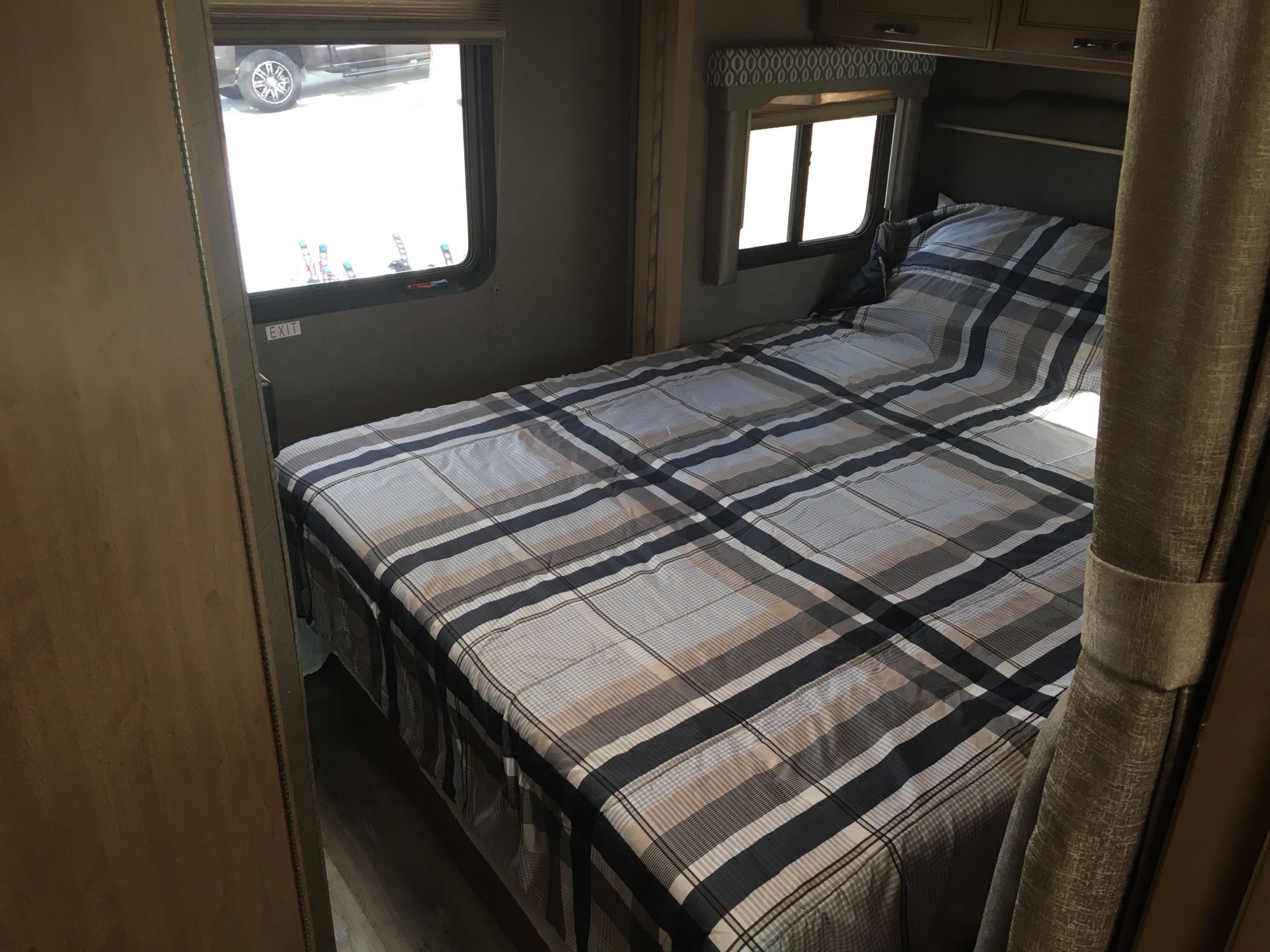 Interior of an RV rental: bedroom with a plaid bed, two windows, and an exit sign below one.. Thor Freedom Elite 2018