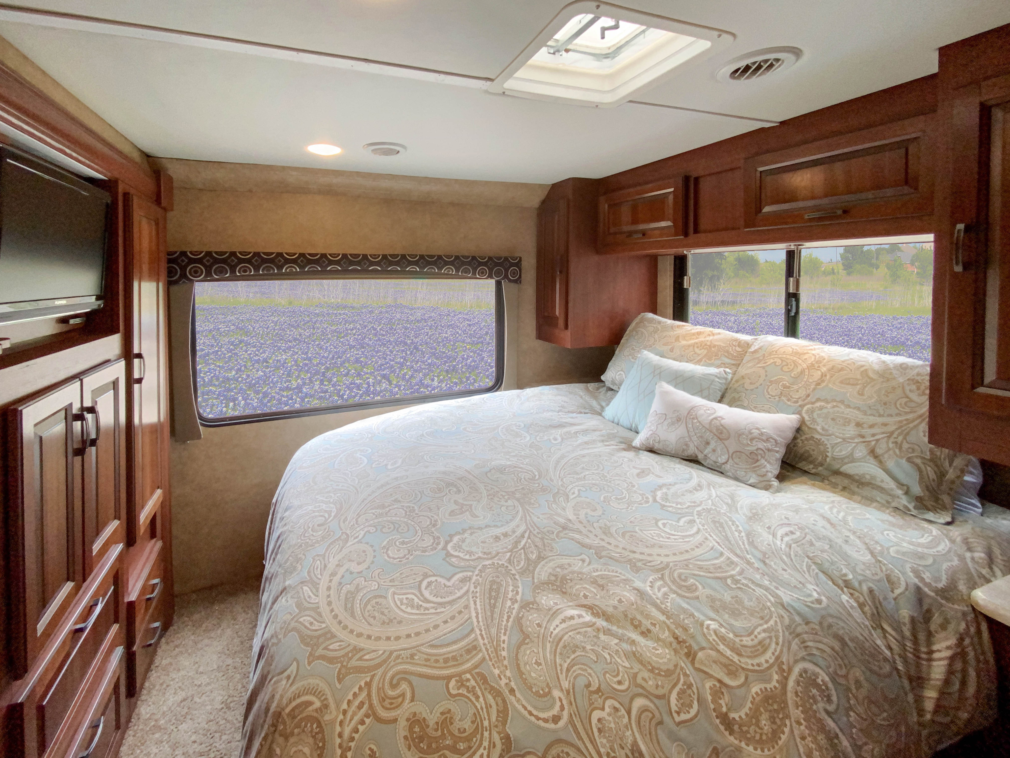 Cozy RV rental bedroom featuring a patterned bed, wood cabinetry, and scenic window views of a vibrant purple flower field.. Forest River Forester 2015