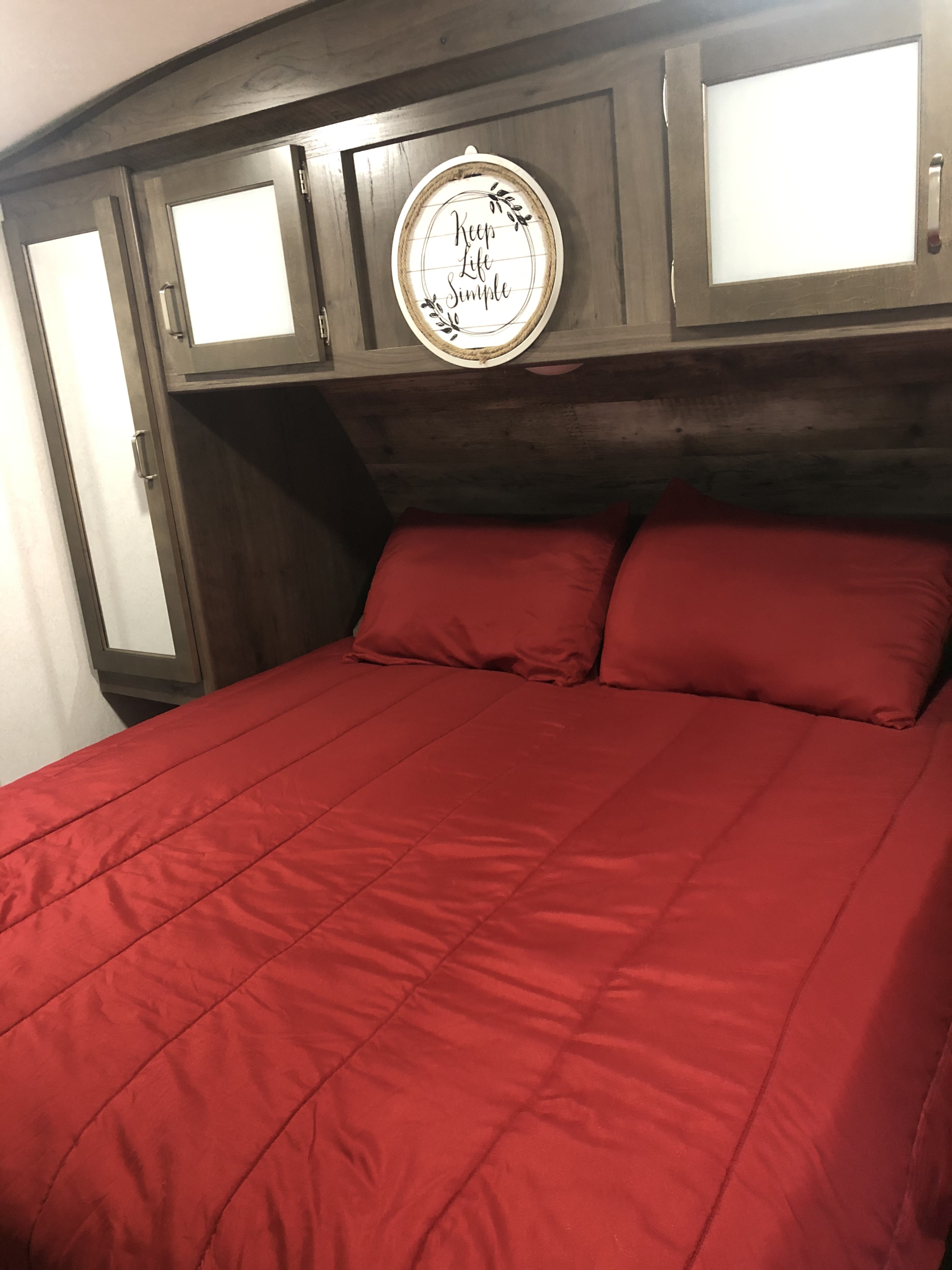 Enjoy this RV rental's bedroom with vibrant red bedding, ample overhead storage, and a welcoming "Keep Life Simple" decor.. Keystone Passport 2020