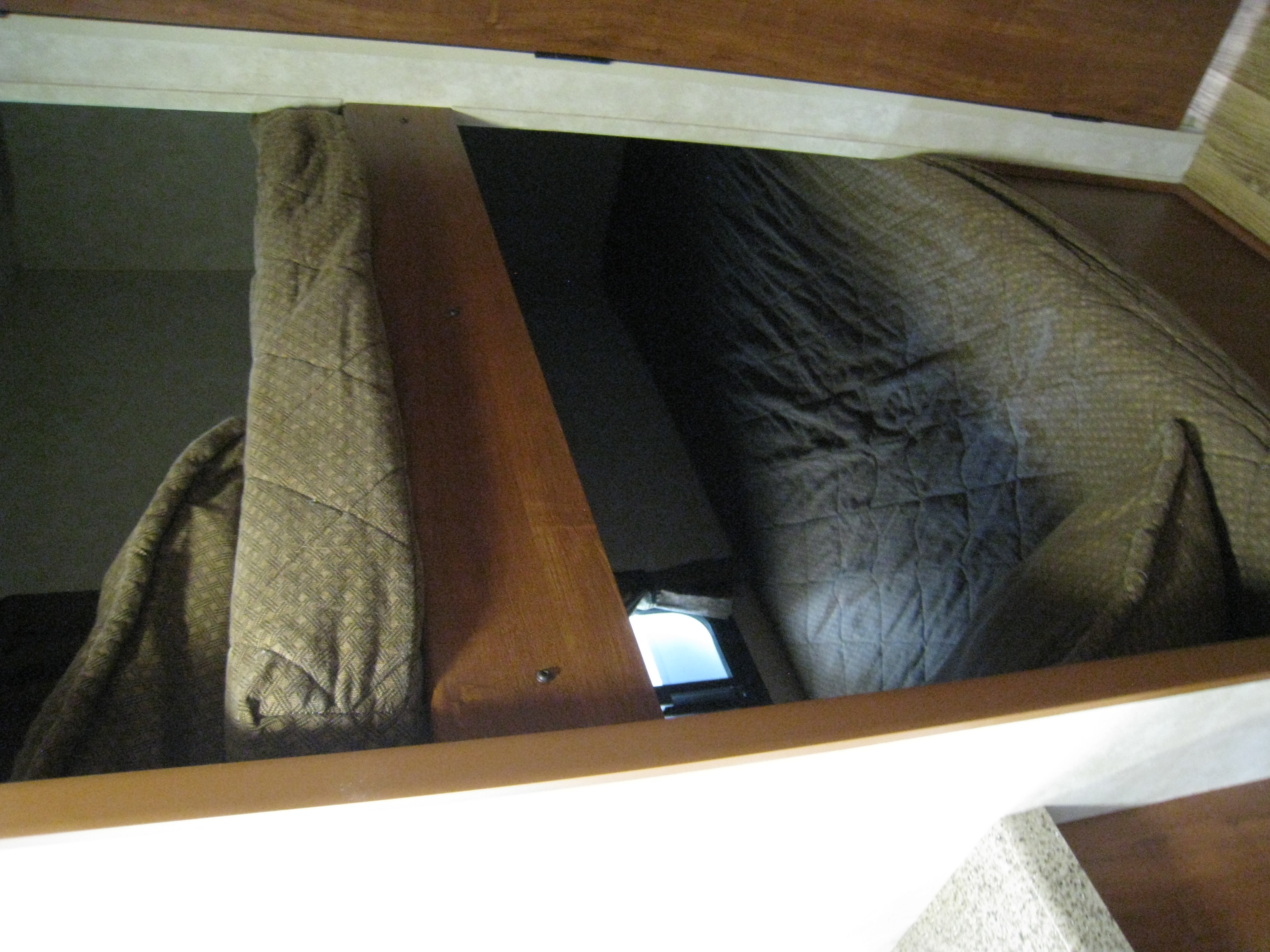 Looking into an RV rental's overhead sleeping area, showing dark quilted bedding on both sides of a wooden divider, with a small window.. Travel Lite Cobblestone I17 2014
