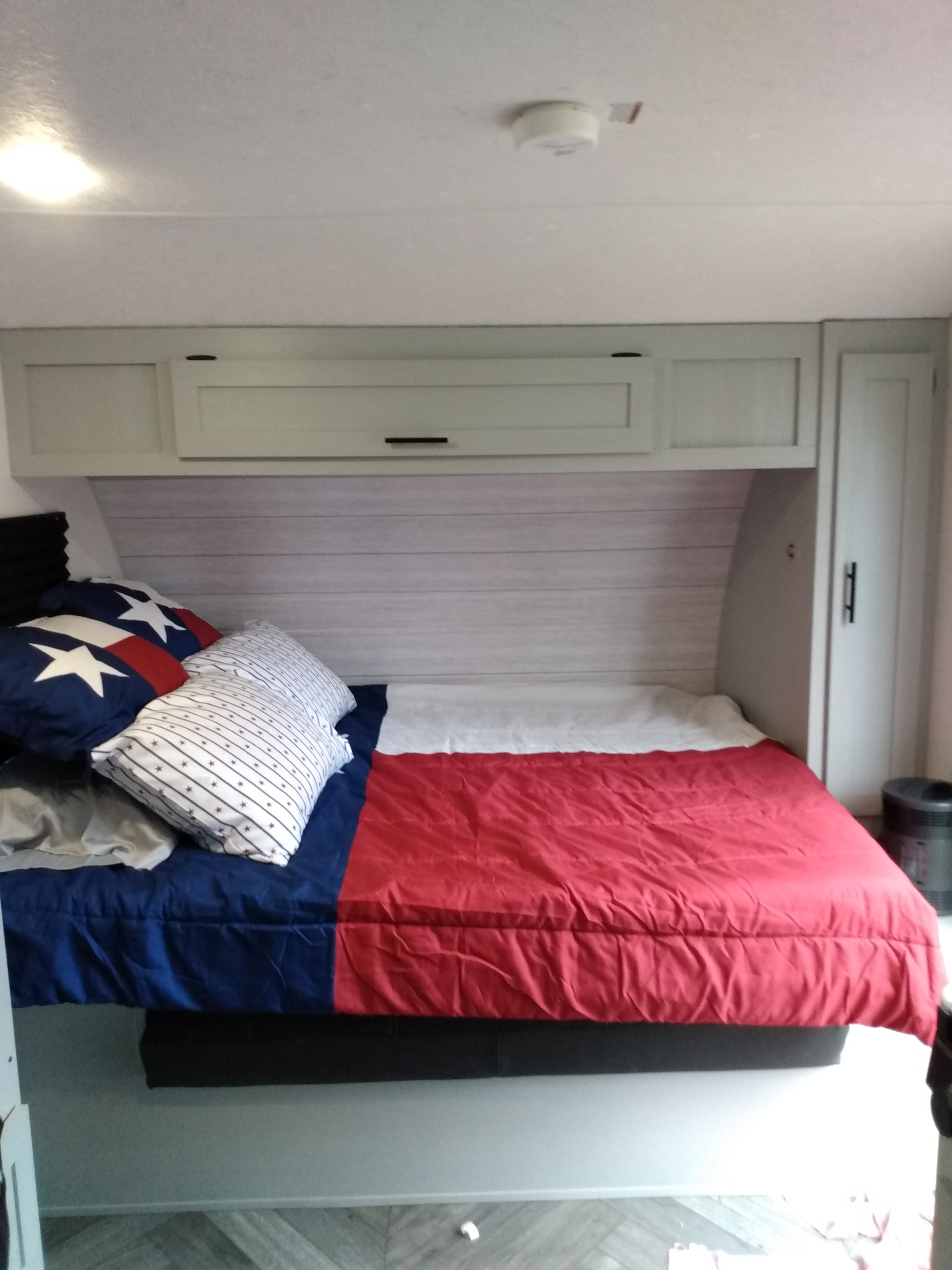 Cozy RV rental bedroom with Texas flag bedding and ample overhead storage.. Forest River Wildwood 2021