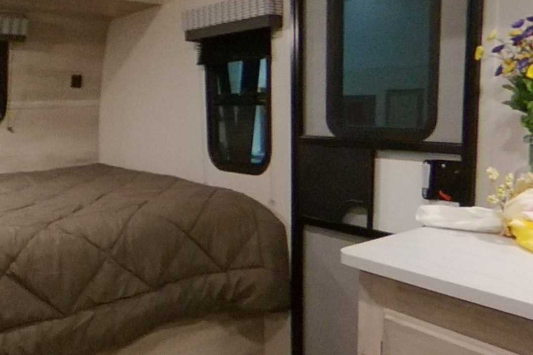 RV rental interior: a comfy bedroom features a quilted bed, two windows with blinds, and a counter.. K-Z Manufacturing Escape 2021