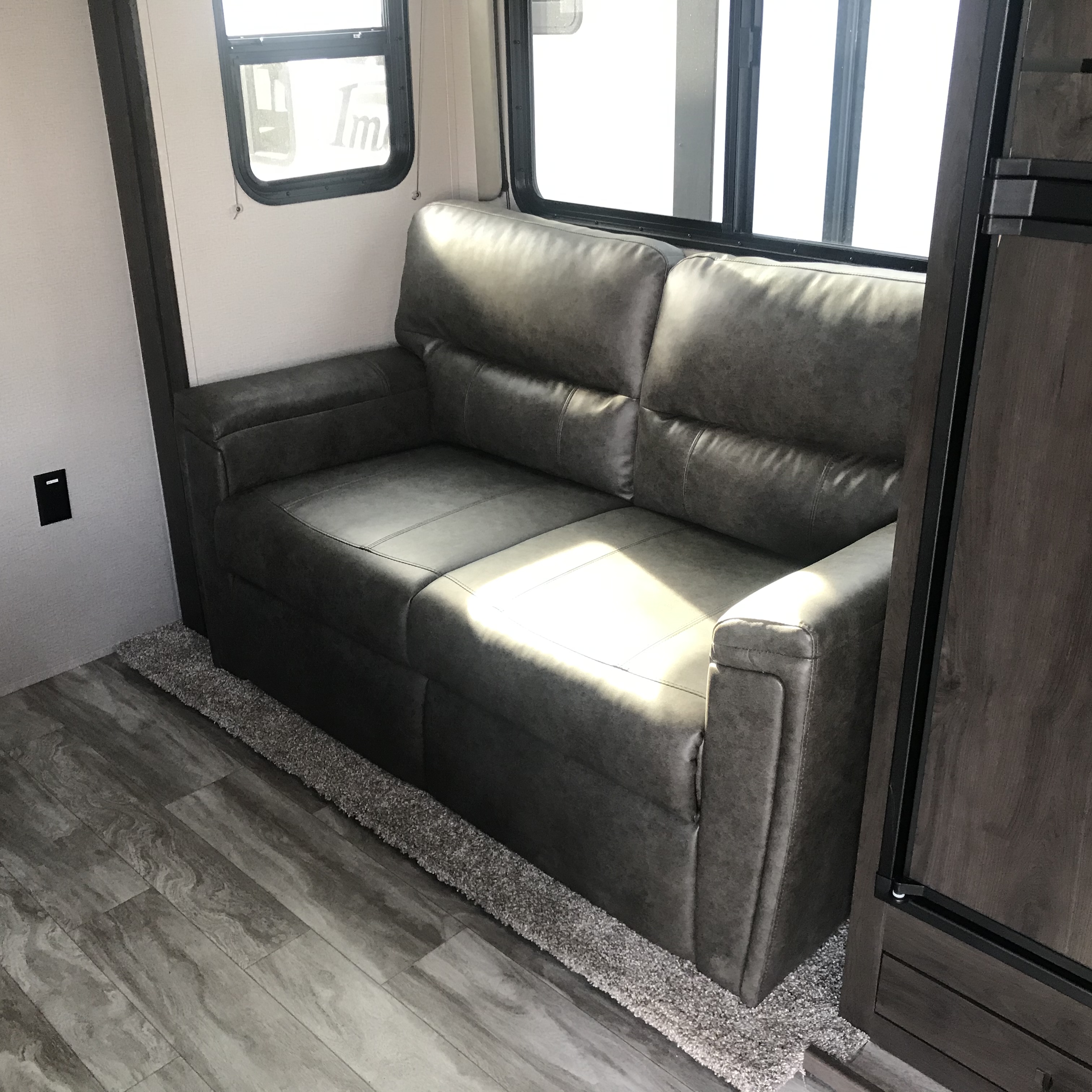 An RV rental interior showing a plush sofa with windows above and wood-look flooring below.. Grand Design Transcend 261BH 2021