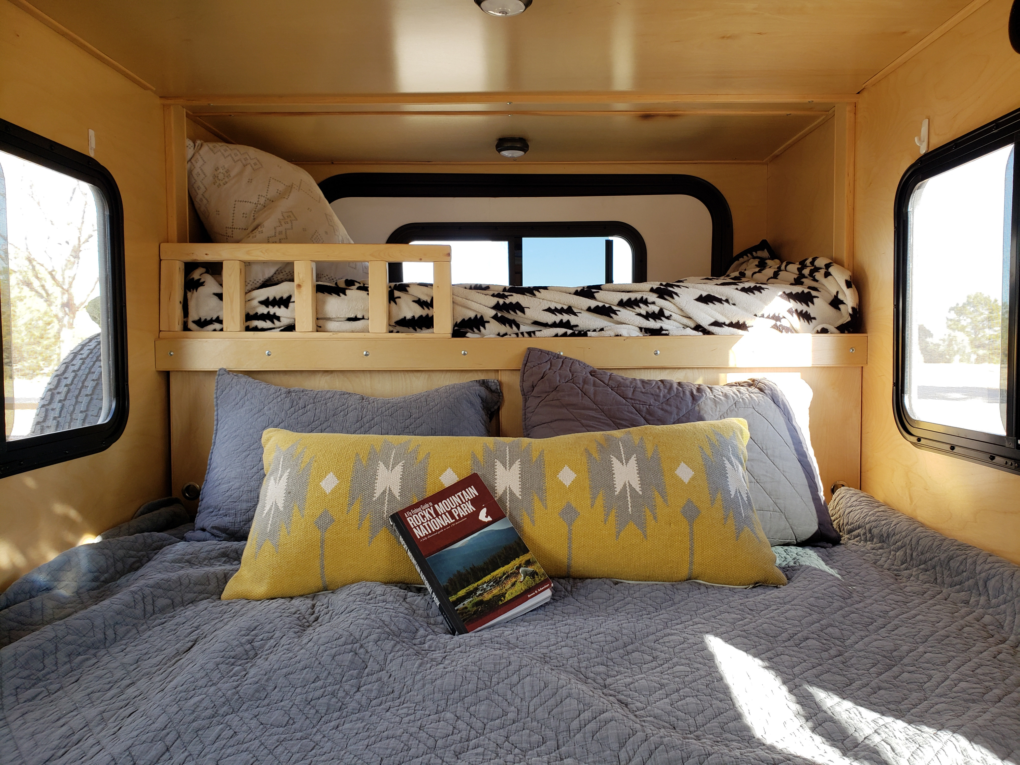 Cozy RV rental interior shows a lower bed with a national park guide, patterned pillows, and a raised bunk bed. Perfect for trips!. Escapade Ridge 2018