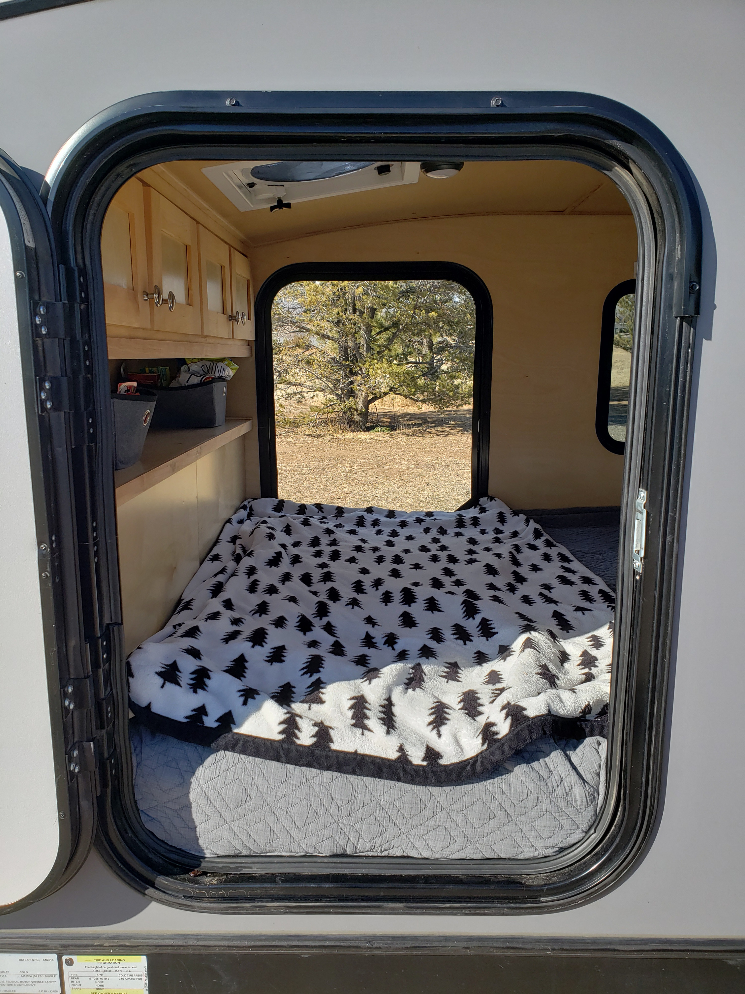 Cozy rv rental interior: A compact camper with a bed, tree-patterned blanket, cabinets, and a window view of nature.. Escapade Ridge 2018