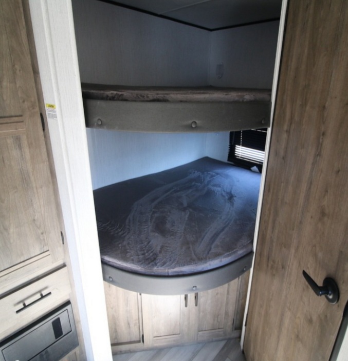 RV rental interior featuring stacked bunk beds: a lower bed with a rounded front and an upper bunk, surrounded by wood cabinetry.. Heartland Pioneer 2021