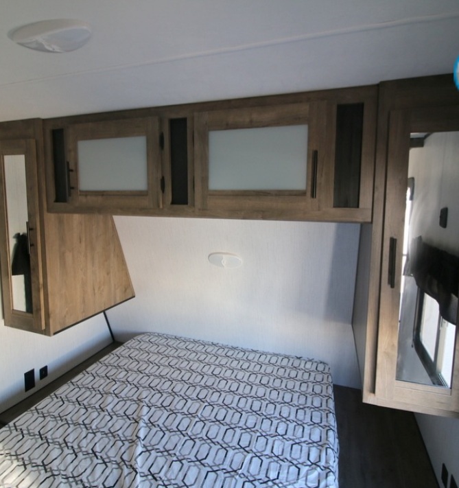 Modern RV rental bedroom: cozy bed with geometric blanket, overhead cabinets, and mirrored side storage for comfortable travel.. Heartland Pioneer 2021