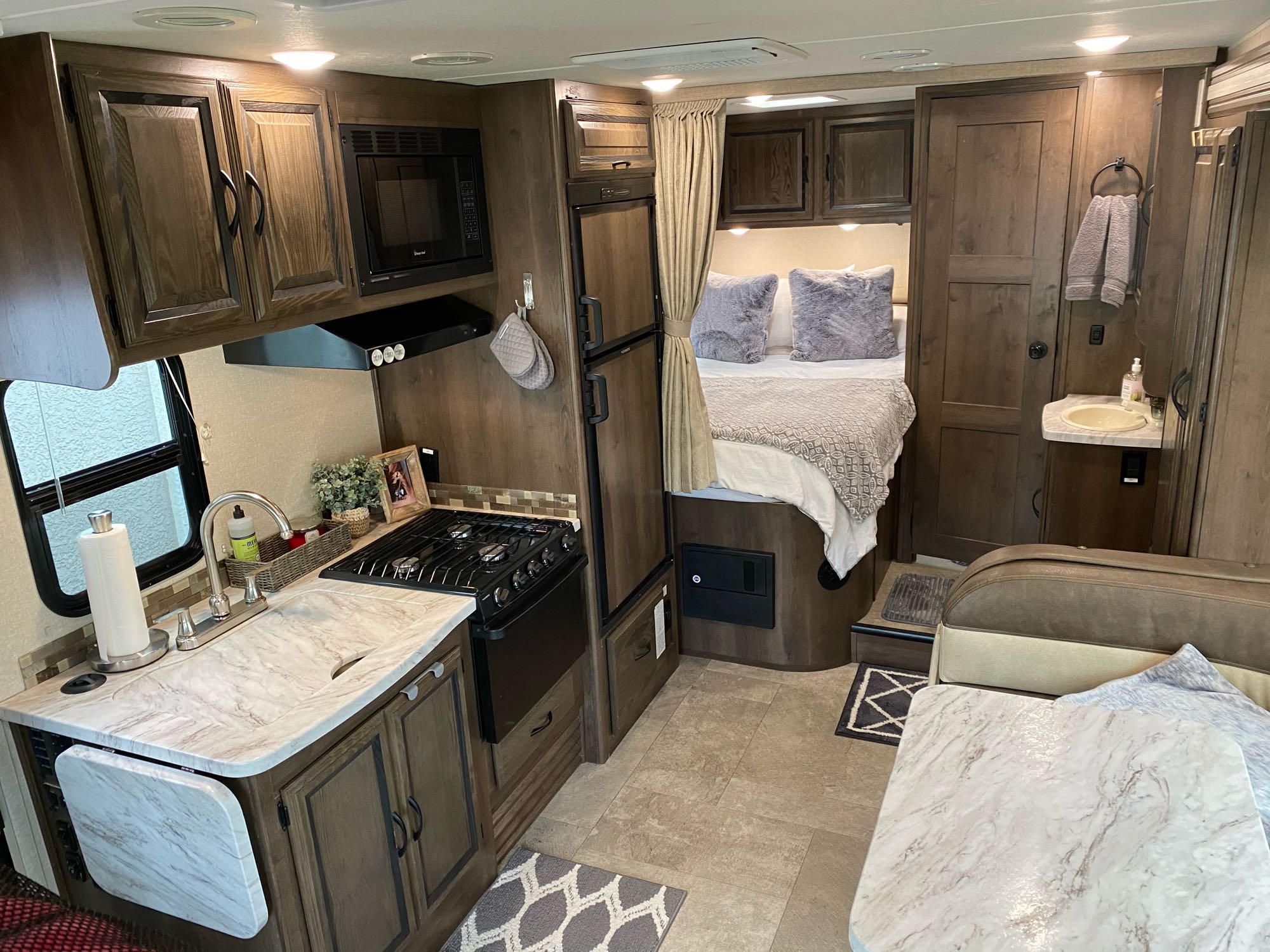 Interior of a modern rv rental: dark wood cabinetry, light countertops, full kitchen, cozy bed, and living area for travel.. Coachmen Prism 2019