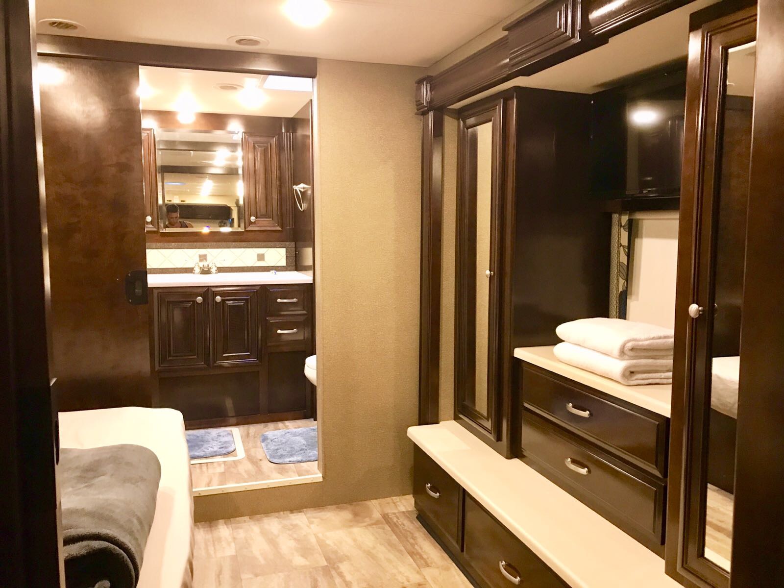 RV rental interior: bedroom with view to spacious bathroom & dark wood storage, stacked towels, TV.. Thor Motor Coach Palazzo 2016
