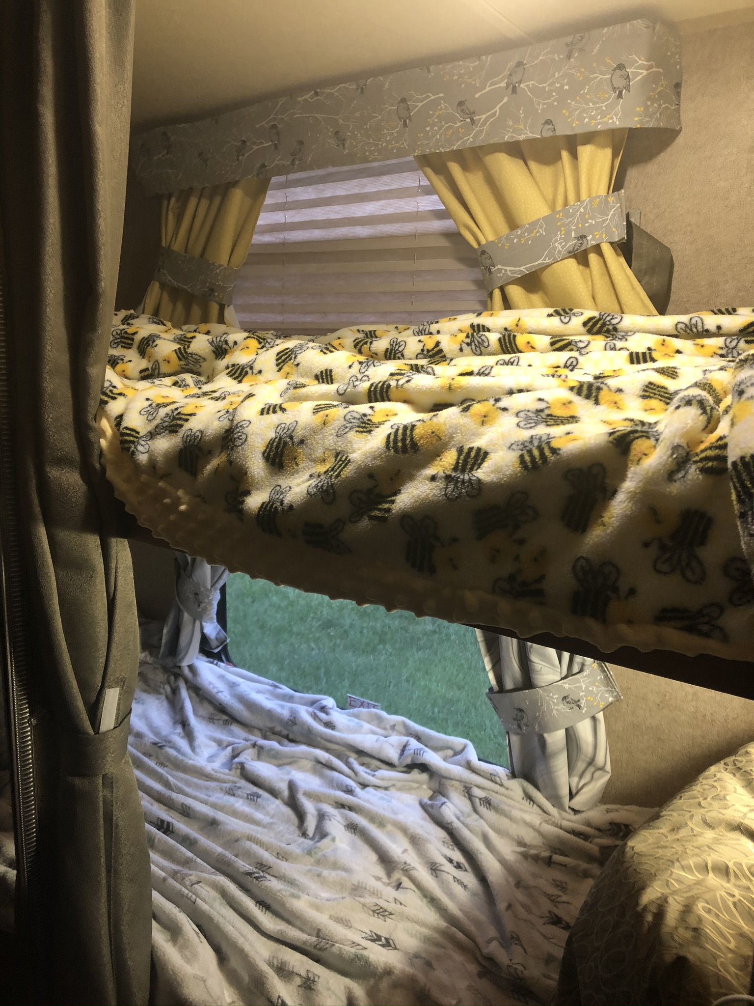 Cozy RV rental bunk beds, with a bee blanket on top and an arrow blanket below, looking out to green grass.. Forest River Rockwood Mini Lite 2015
