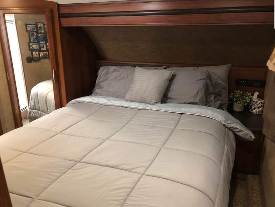 This cozy RV rental bedroom features a comfortable bed with gray bedding, a mirrored closet, and a nightstand.. Forest River Crusader 2015