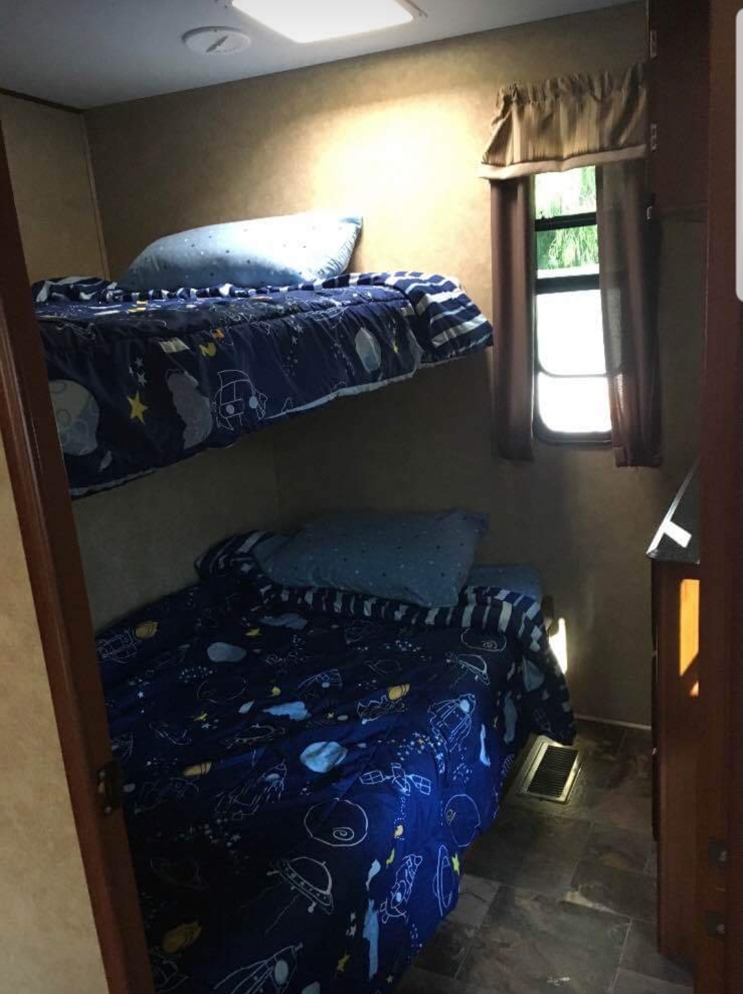Explore this RV rental's cozy bedroom featuring two space-themed bunk beds, window, and wood-look flooring.. Forest River Crusader 2015