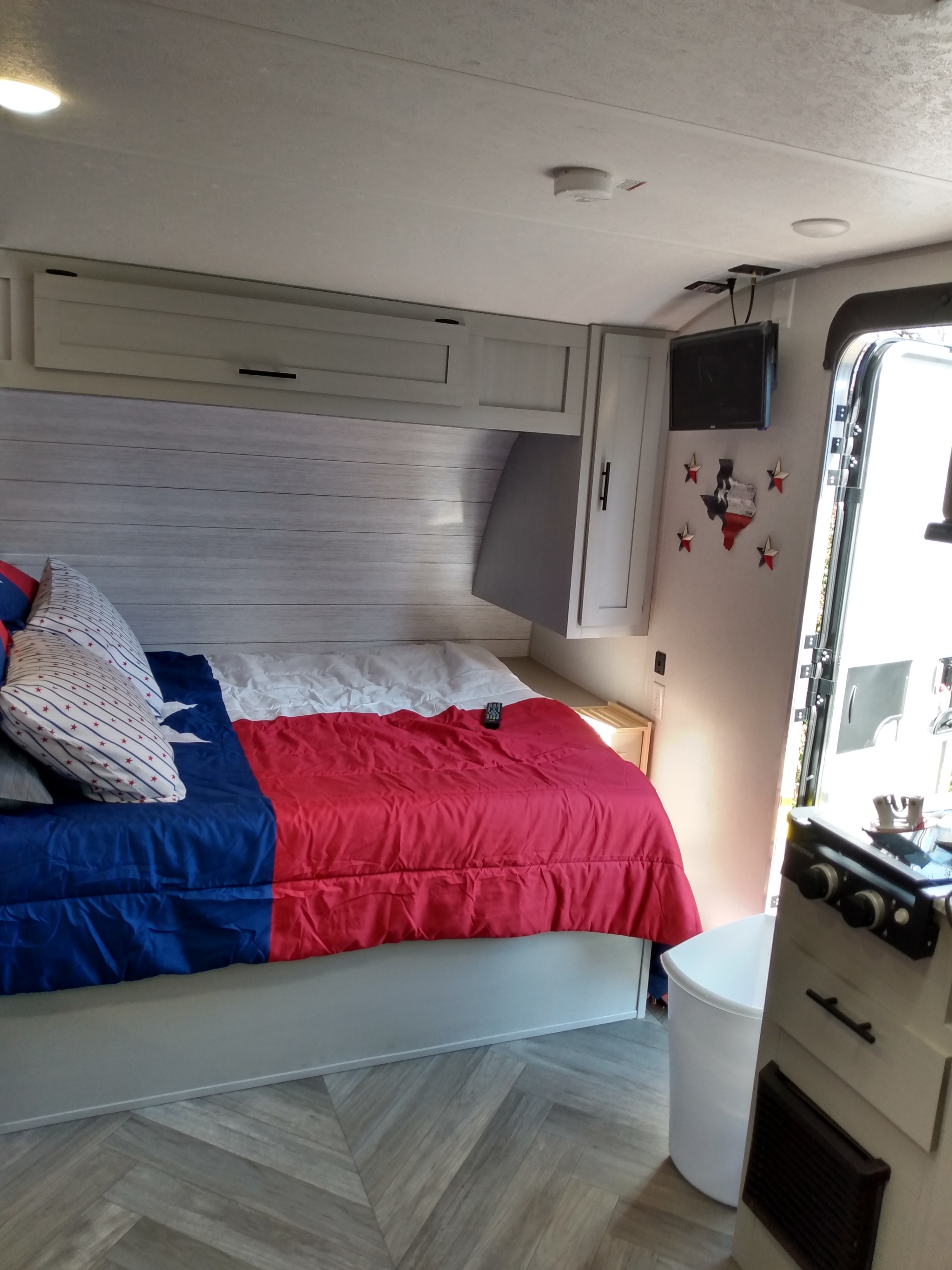 RV rental interior featuring a bed with Texas flag bedding, modern light wood walls, flooring, and a mounted TV.. Forest River Salem 2021