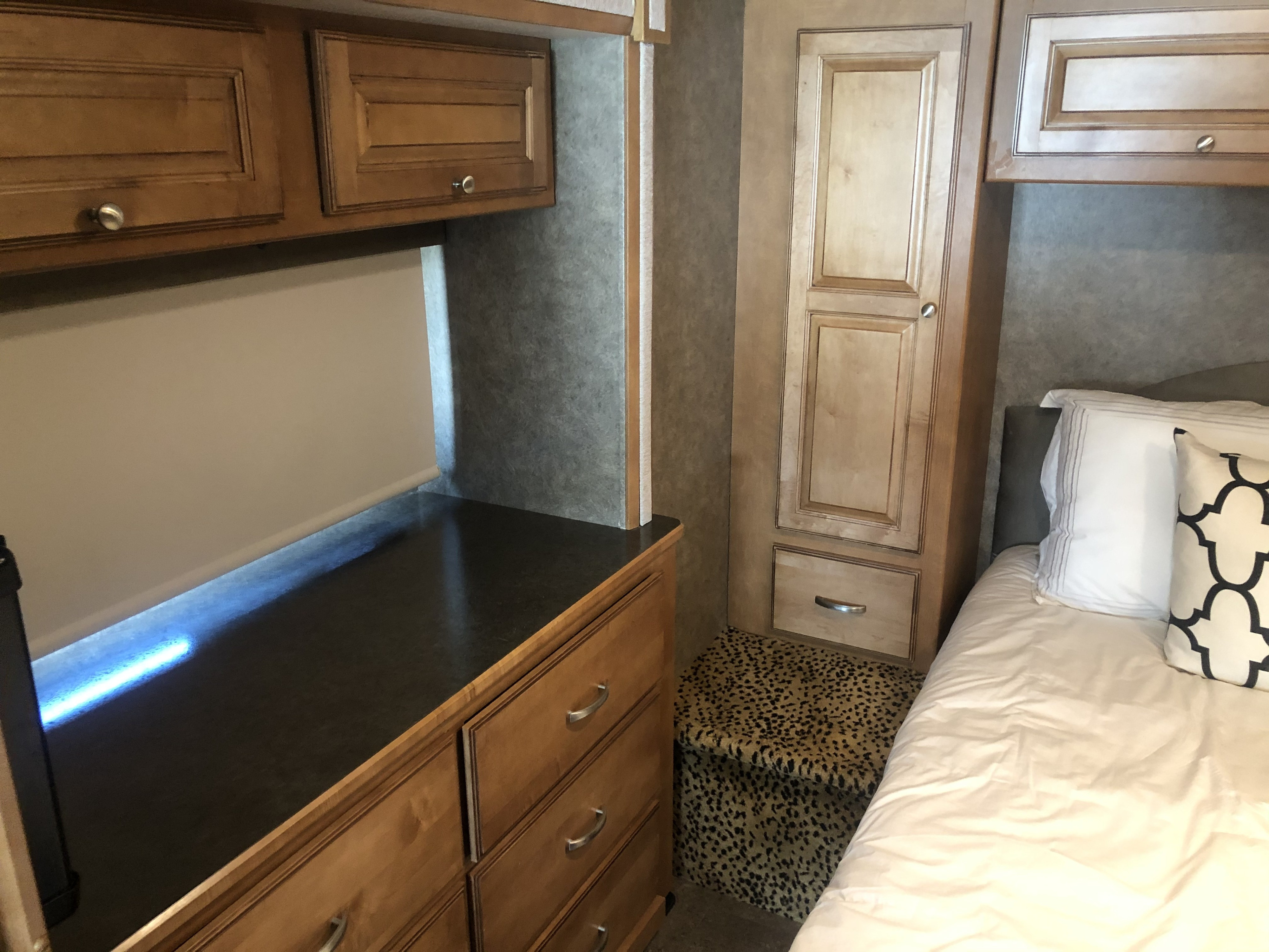 RV rental bedroom with wooden cabinets, a desk with blue under-lighting, a bed, and leopard print storage ottoman.. Itasca Sunstar 2015