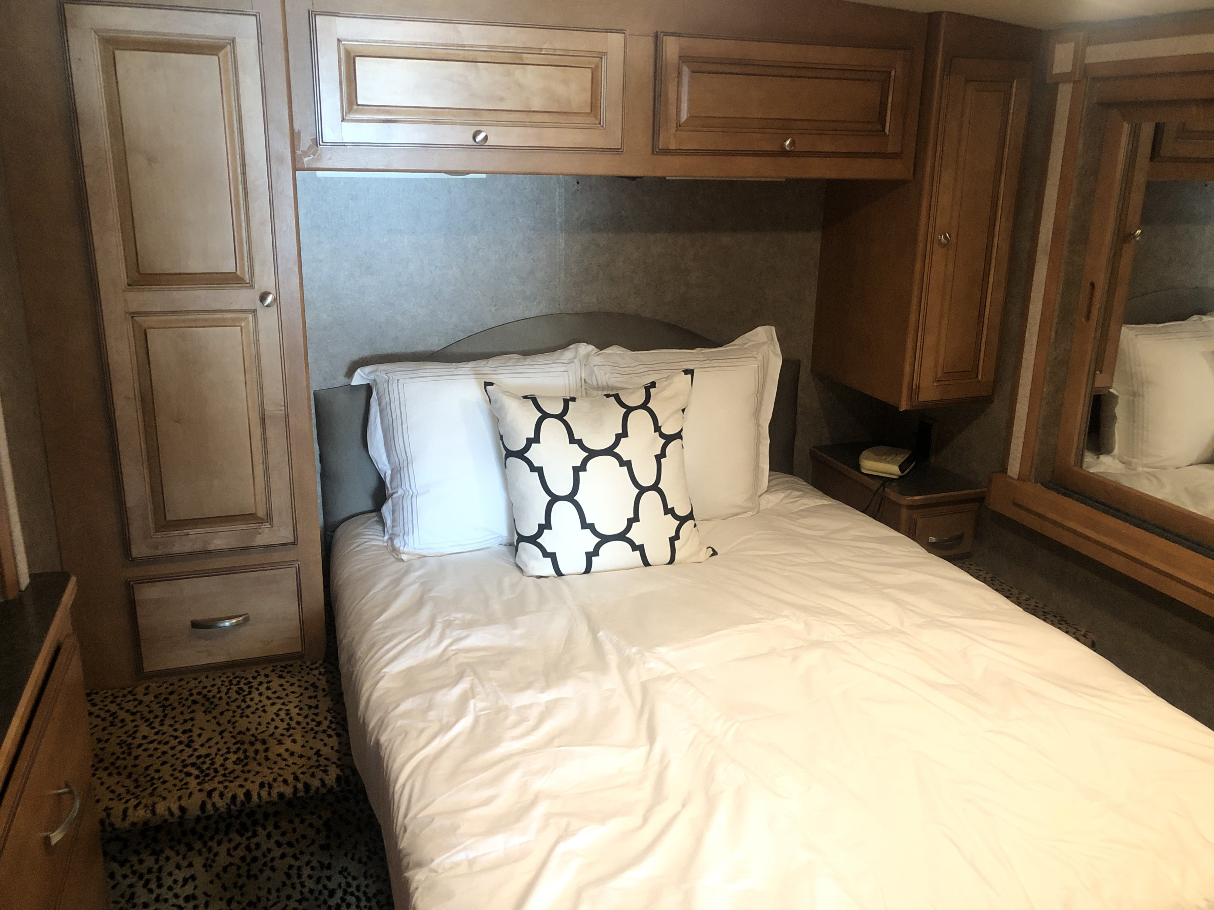 Inside a cozy RV rental: a comfortable bed with white linens, surrounded by wood cabinets & storage.. Itasca Sunstar 2015