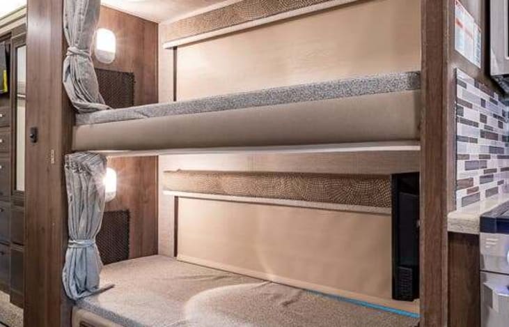 RV rental interior showing comfortable bunk beds. Each bunk has privacy curtains and lights, ideal for family travel.. Entegra Coach Esteem 2021