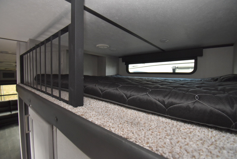 Cozy RV rental loft bed: black quilted mattress, light carpet, safety railing, and small window for a comfortable stay.. Other Other 2022