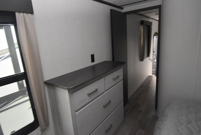 Compact RV rental bedroom featuring a dresser and window, with an adjacent hallway. Efficient space for mobile travel.. Other Other 2022