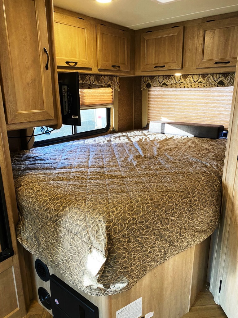 Cozy RV rental bedroom with a large, patterned bed, light wood overhead cabinets, and a mounted TV.. Forest River Coachmen Freelander 2016