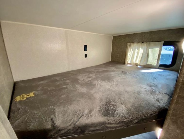 RV rental bunk bed: Spacious sleeping area with a window and curtains, providing comfort for travel.. Highland Ridge RV Open Range 2021