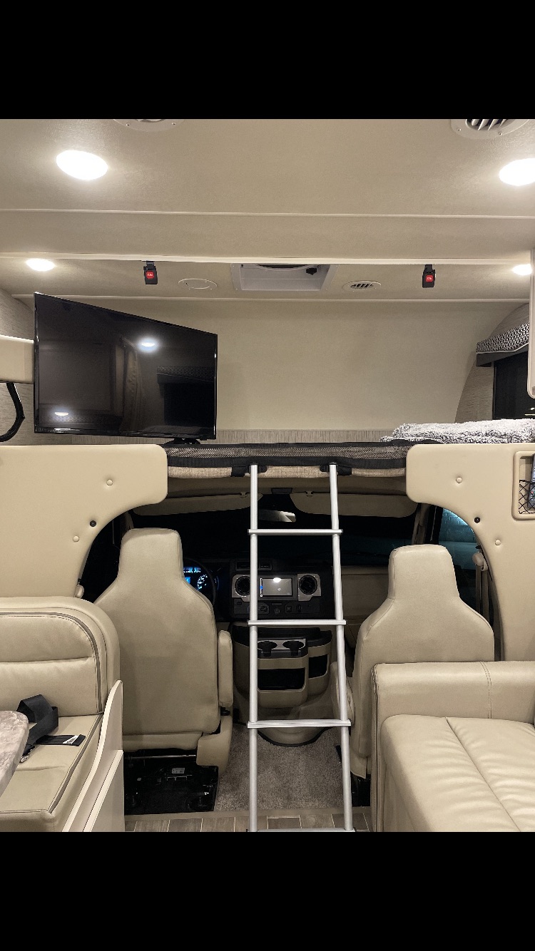 Inside an RV rental: a cozy overhead bunk bed with ladder, flat-screen TV, and lounge area. Ready for your adventure.. Thor Motor Coach Chateau 2021