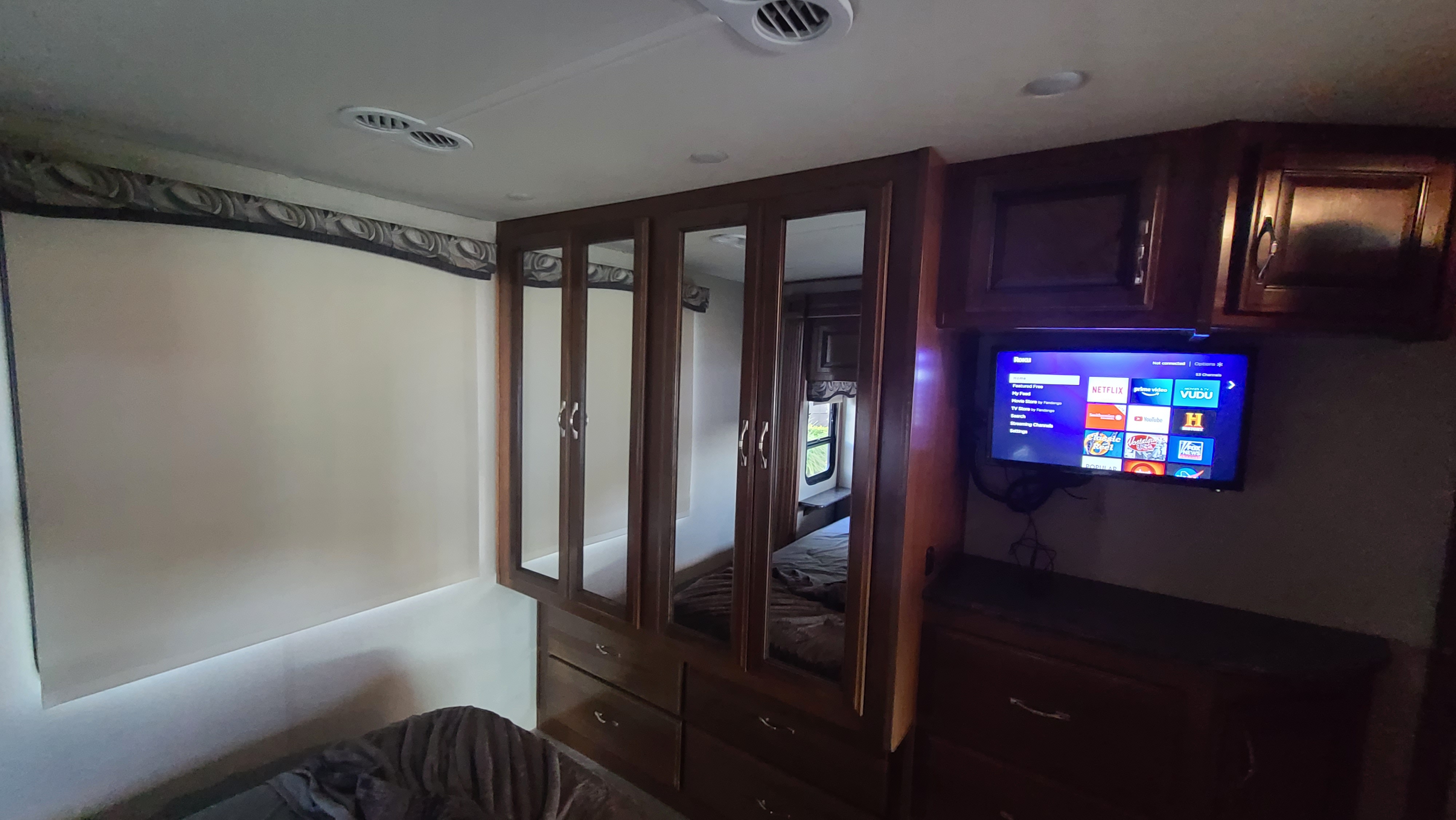Inside an RV rental bedroom: a mounted TV displaying Roku, built-in mirrored wardrobe, and a cozy bed for rest.. Fleetwood Flair 2017