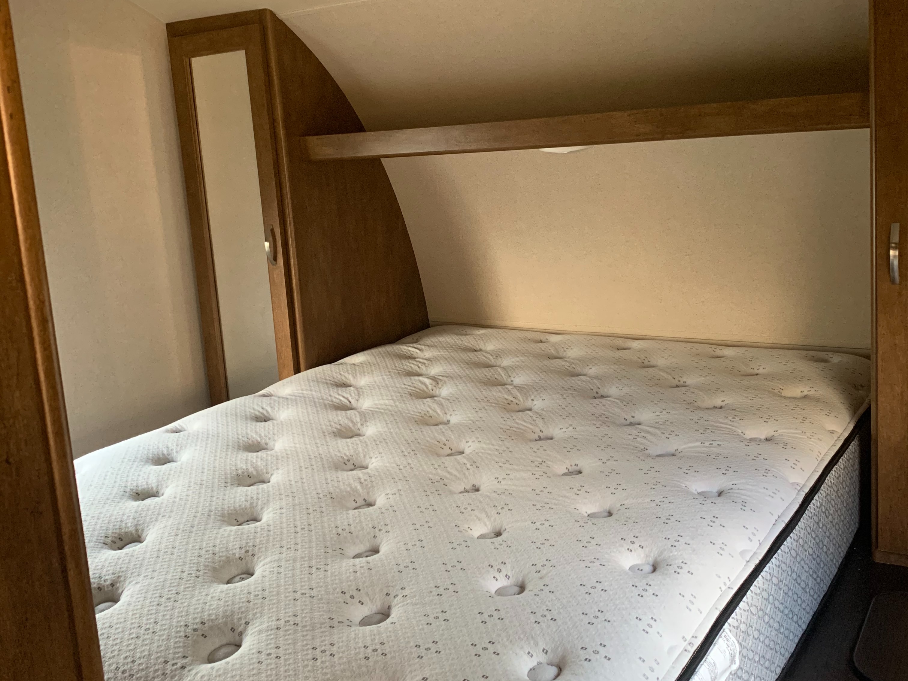 Cozy RV rental bedroom showing a clean mattress, wooden cabinets, and an overhead shelf for travelers.. Forest River Salem 2018