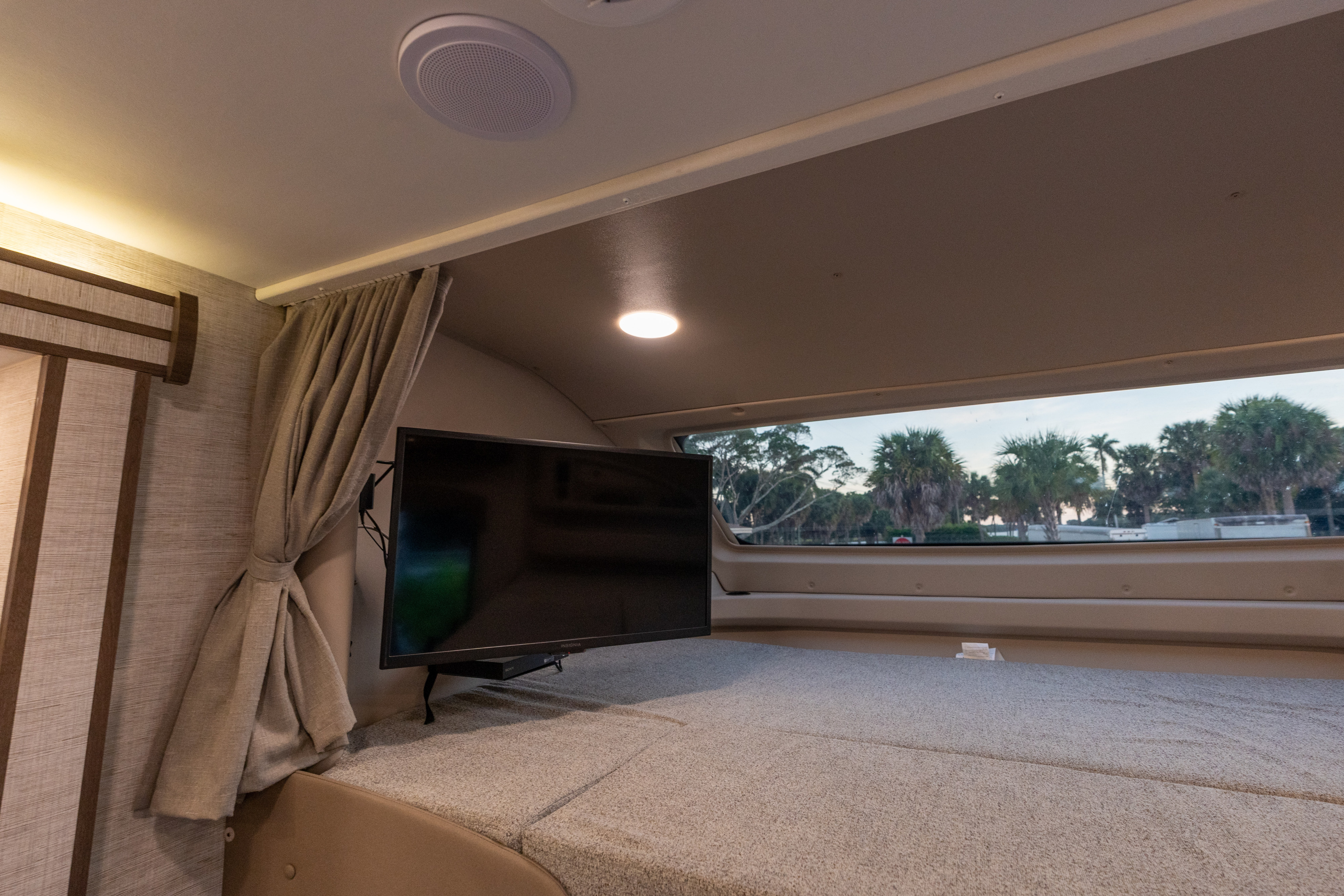 Cozy RV rental interior featuring a bed, TV, and window view of palm trees. Ideal for a comfortable travel experience.. Entegra Coach Esteem 31F 2021