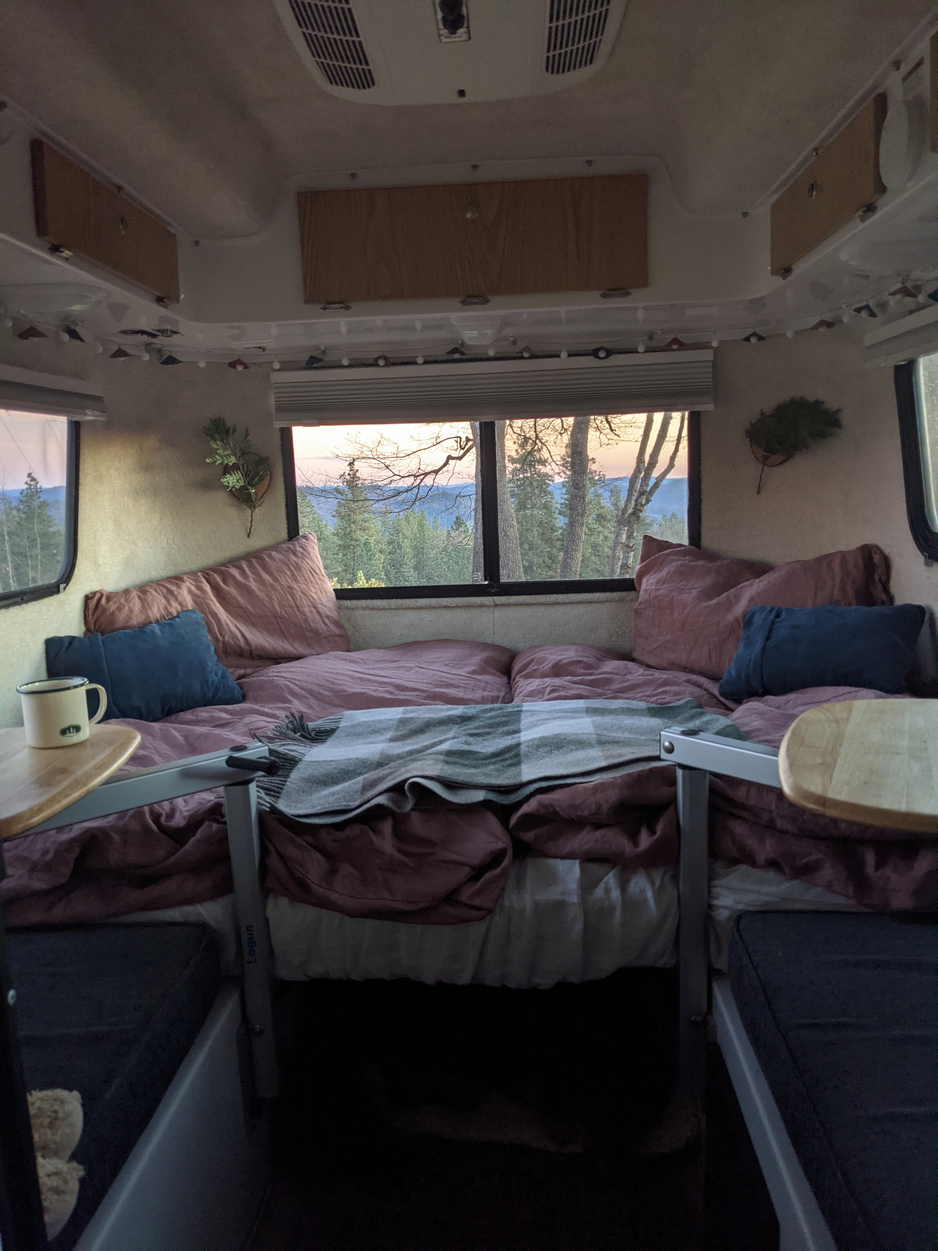Cozy RV rental interior with a comfortable bed, tables, and a scenic window view of a forest and sunset.. Casita Casita Trailer 2015