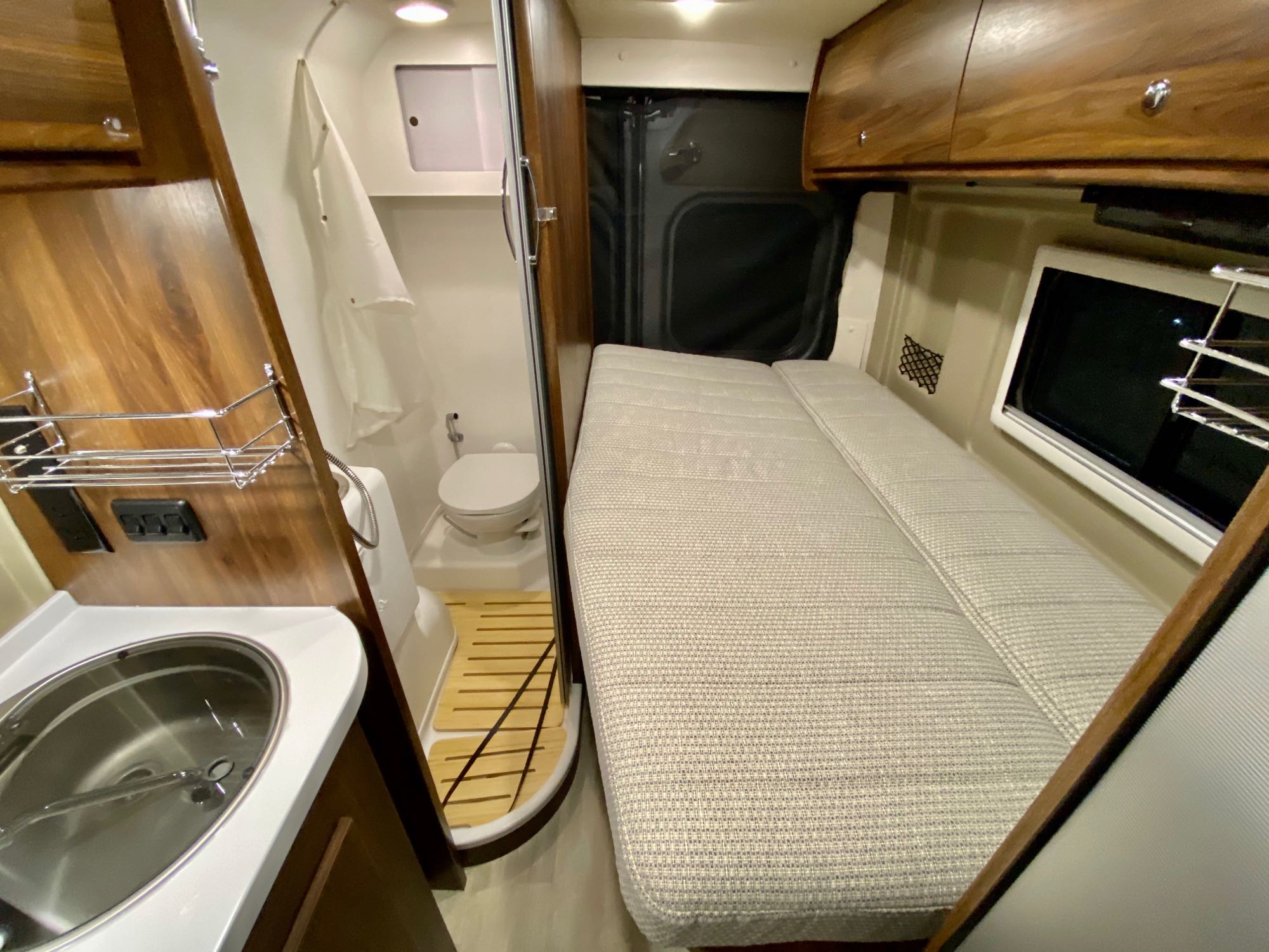 This RV rental interior features a compact sink, wet bath with toilet, and cushioned bed/seating area.. Winnebago Travato 2021